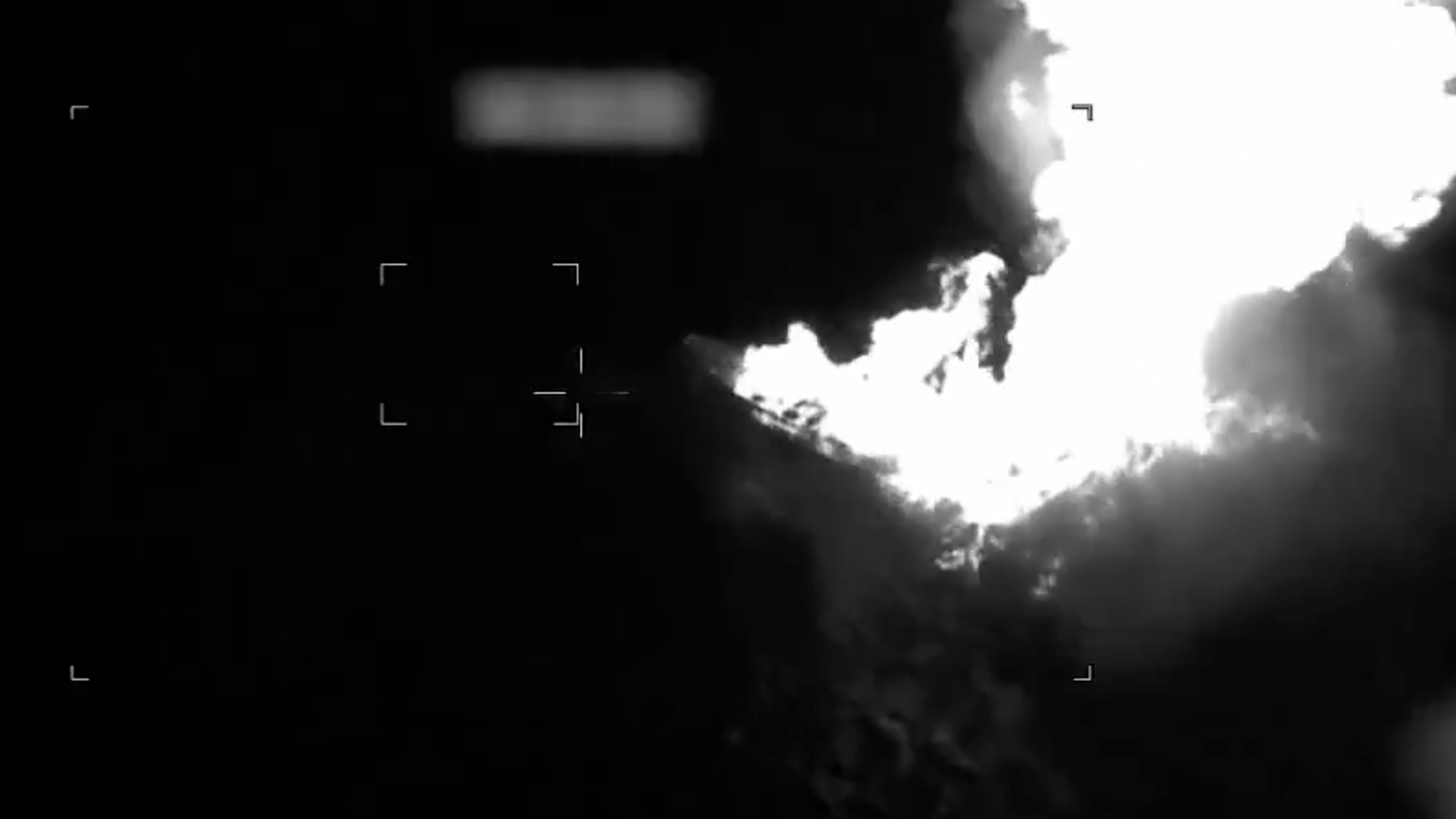 A night-vision style image with a dark background and a bright white explosion or fireball on the right.