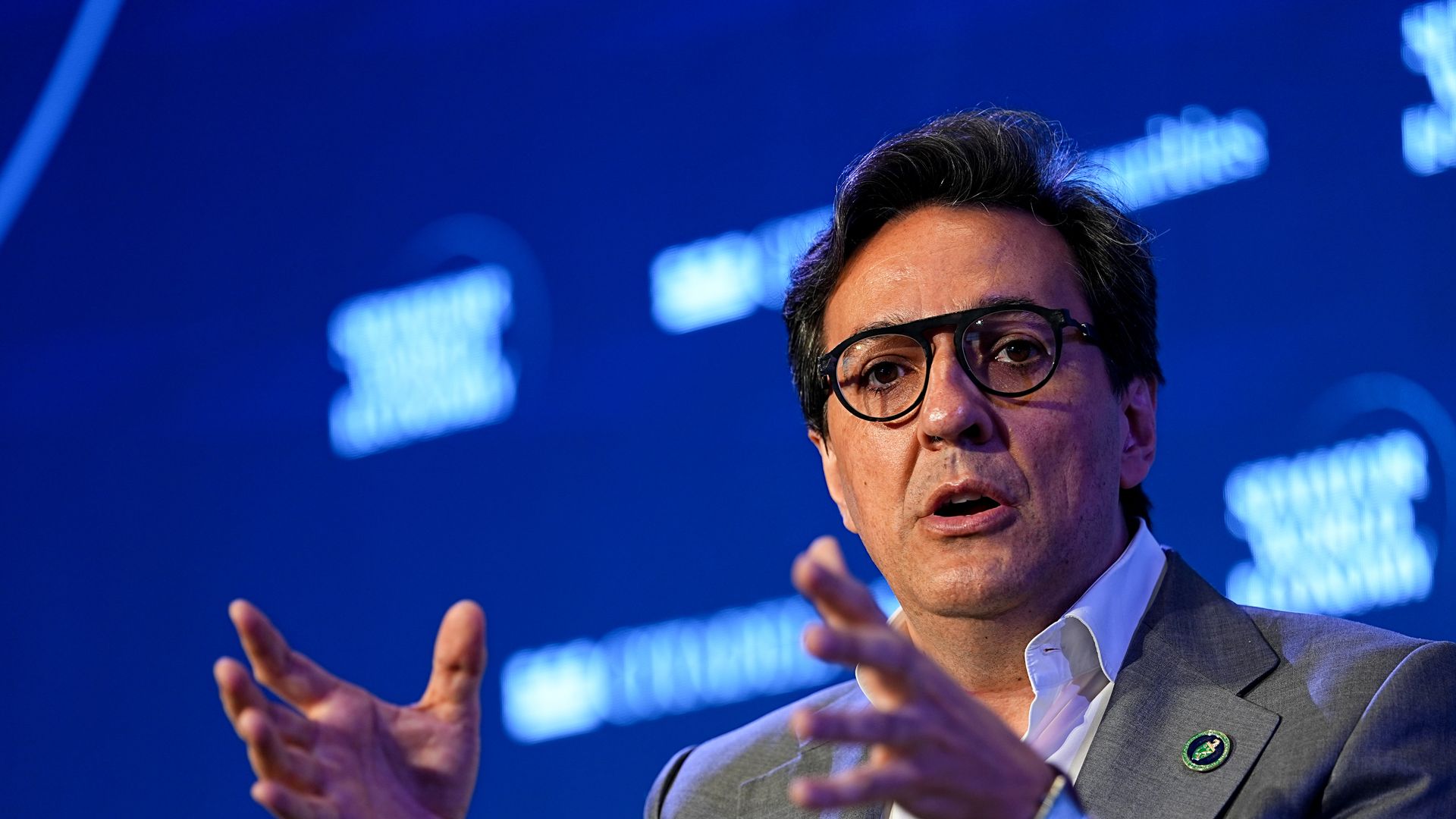 A person with glasses gesticulates with their hands while speaking