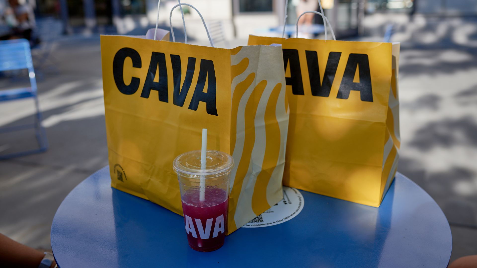 Two Cava yellow bags with a clear Cava cup on a blue table