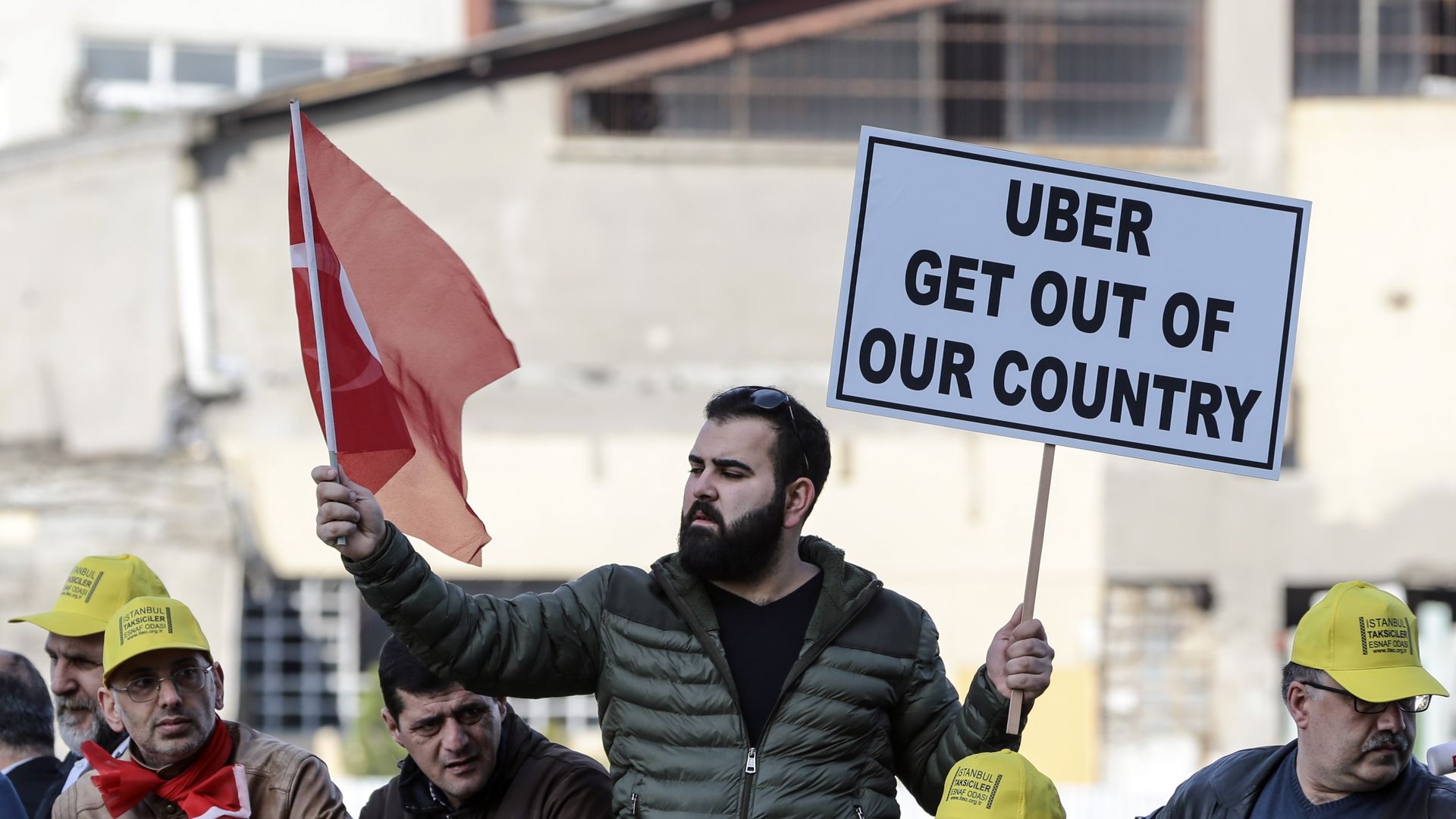 Man holds a Turkish flag in one hand and a sign that reads "Uber get out of our country" in the other.