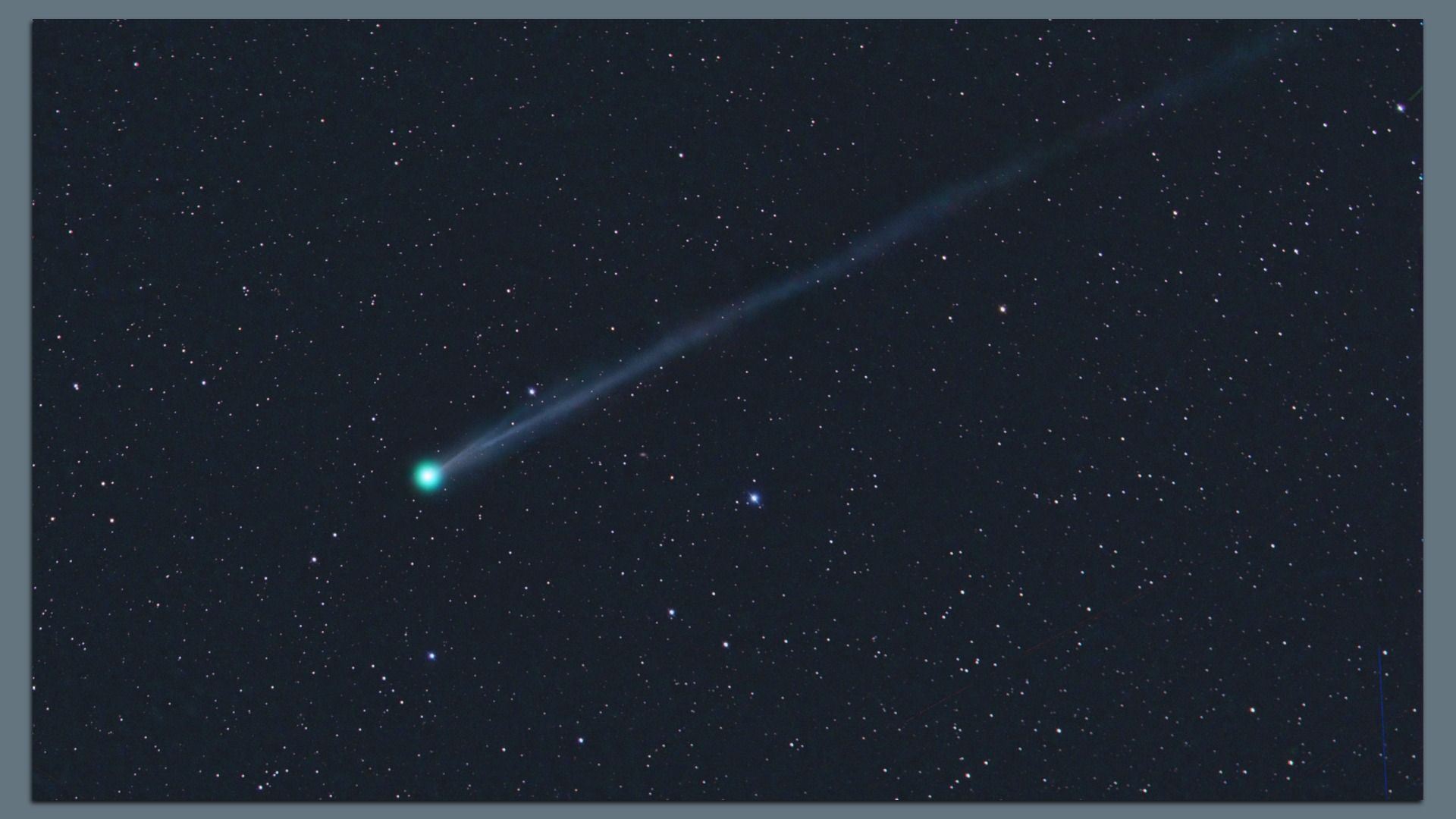 A green comet streaks through the dark sky. 