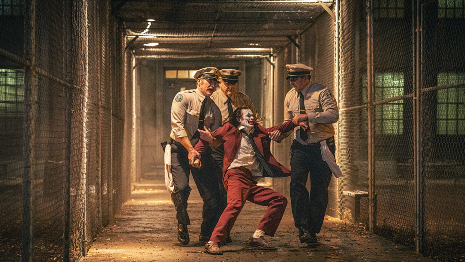still photo from the film "Joker 2" where Joaquin Phoenix in costume is being dragged by police officers