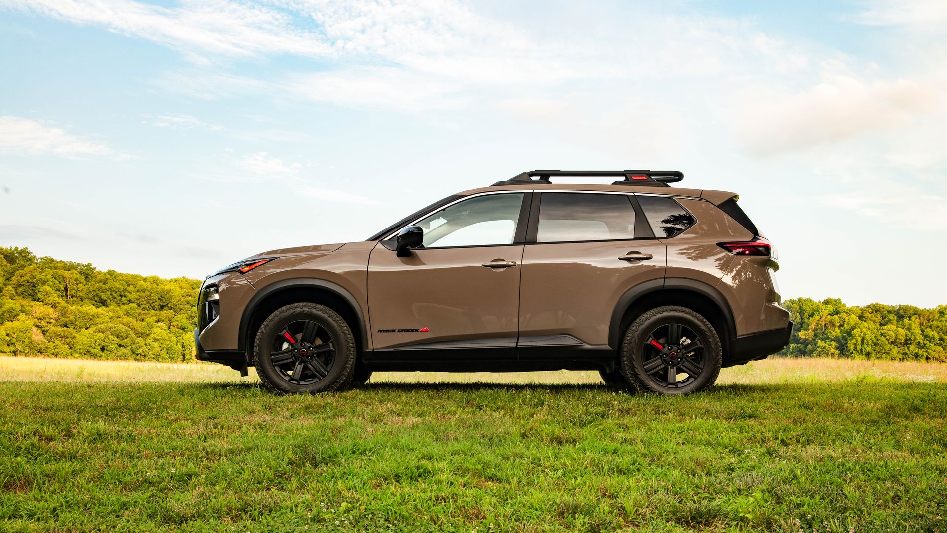 Image of a beige 2025 Nissan Rogue Rock Creek edition parked in a green field. 