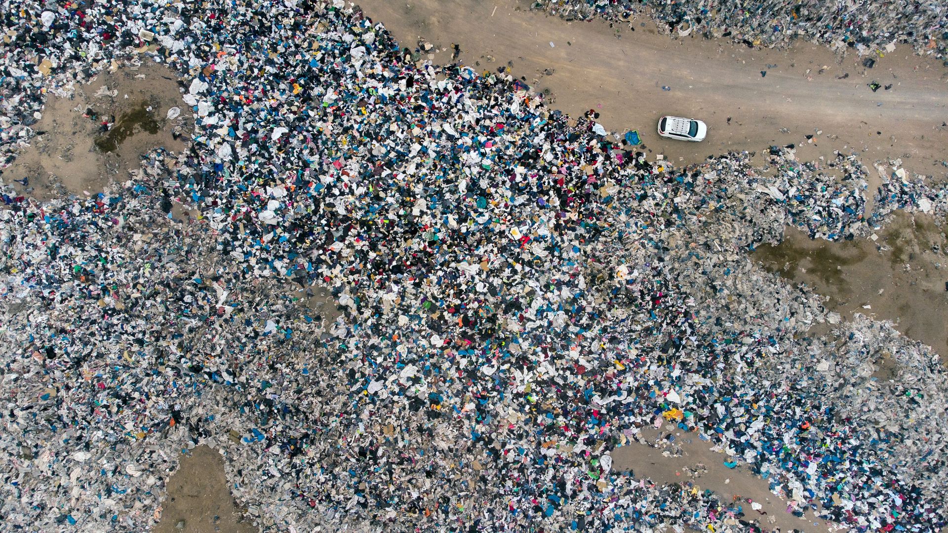 Tons of discarded clothing are piled up on a Chilean desert as a car drives through a dirt road