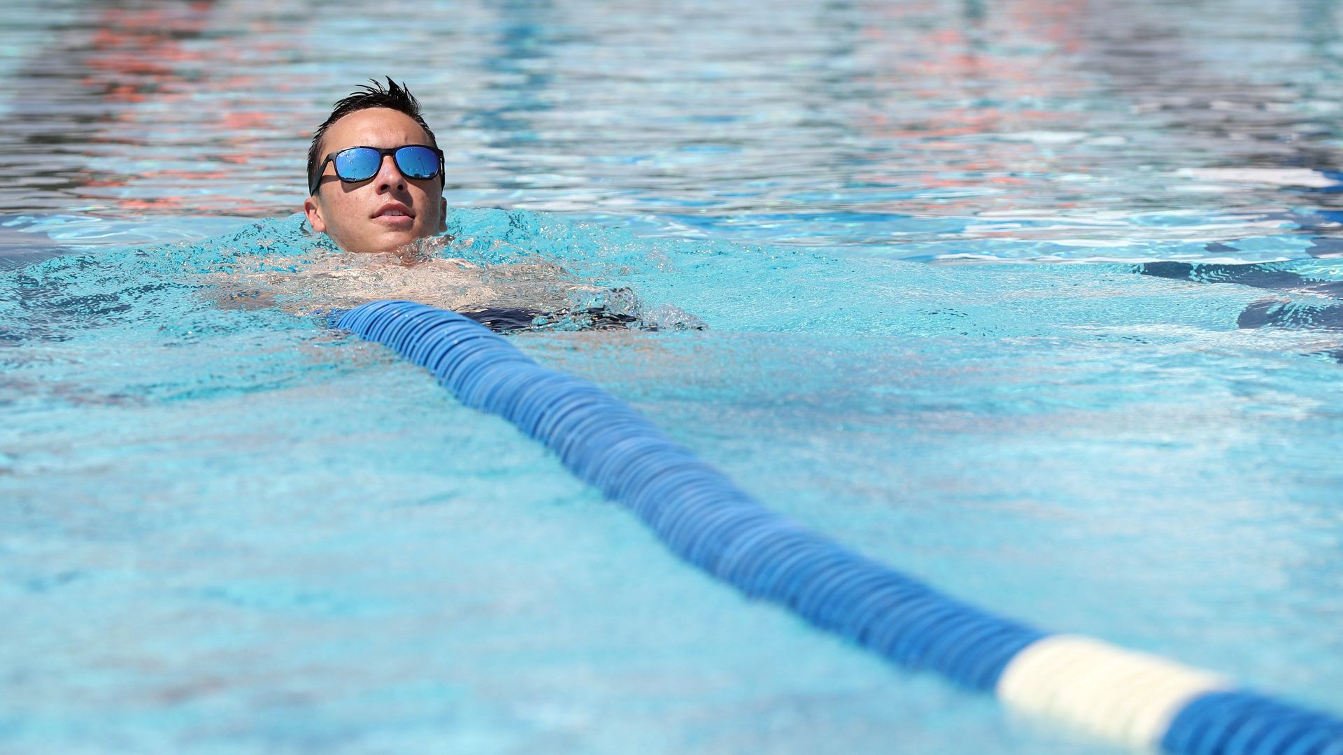 A lifeguard swims while setting up a pool's lap lane.