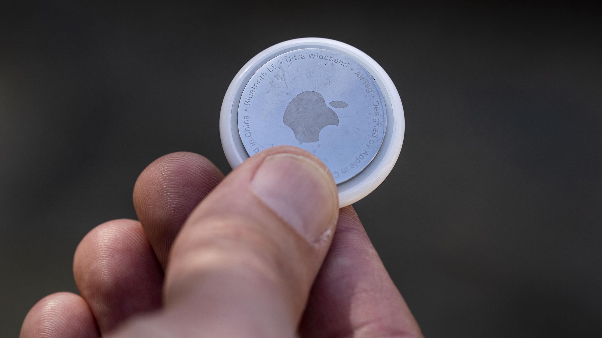 A person holds an Apple AirTag in between their fingers.