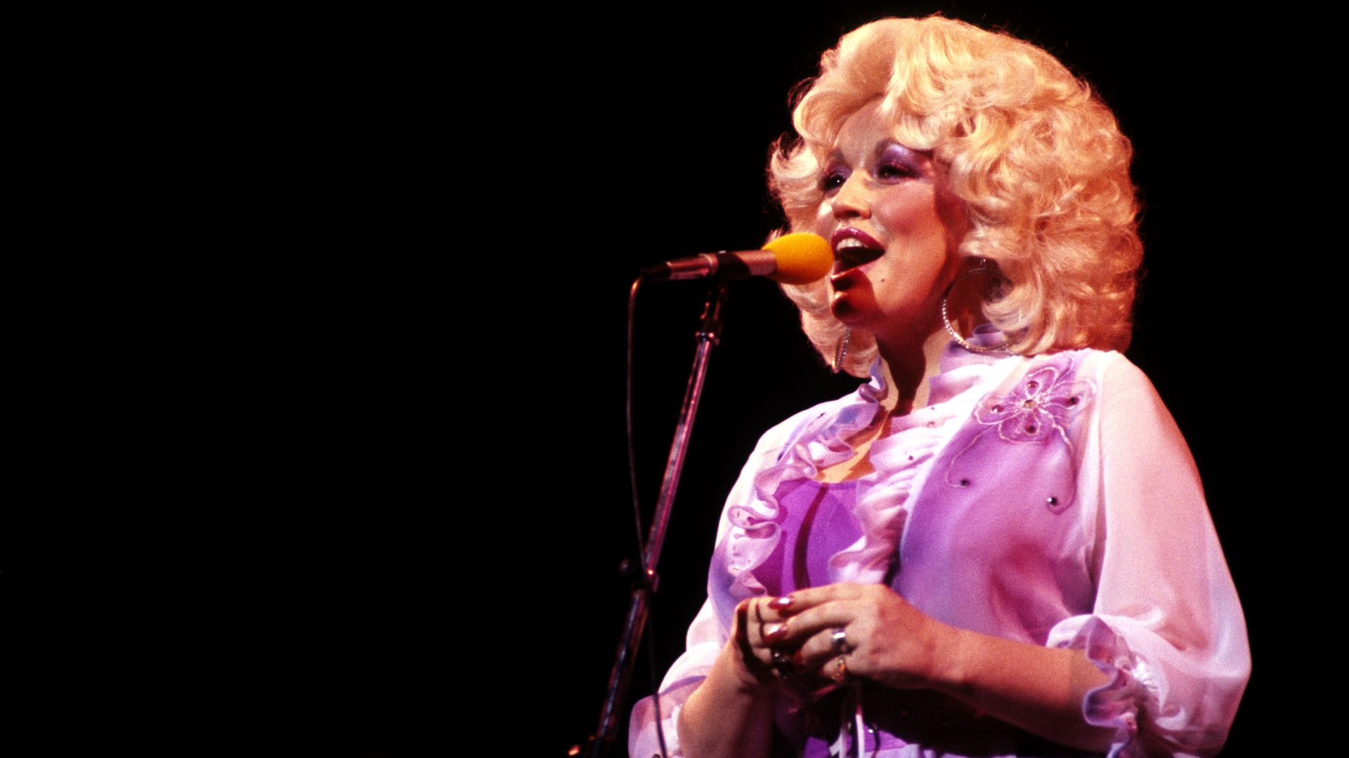 Dolly singing onstage in front of a microphone.