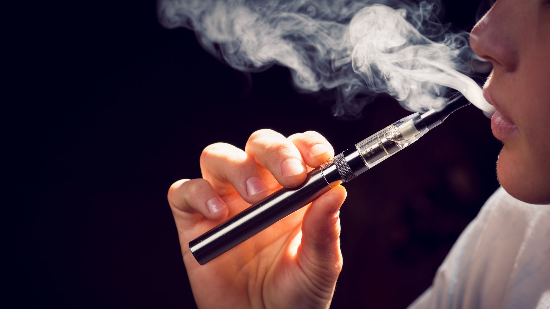 In this image, a young person holds an e-cigarette and vapes.