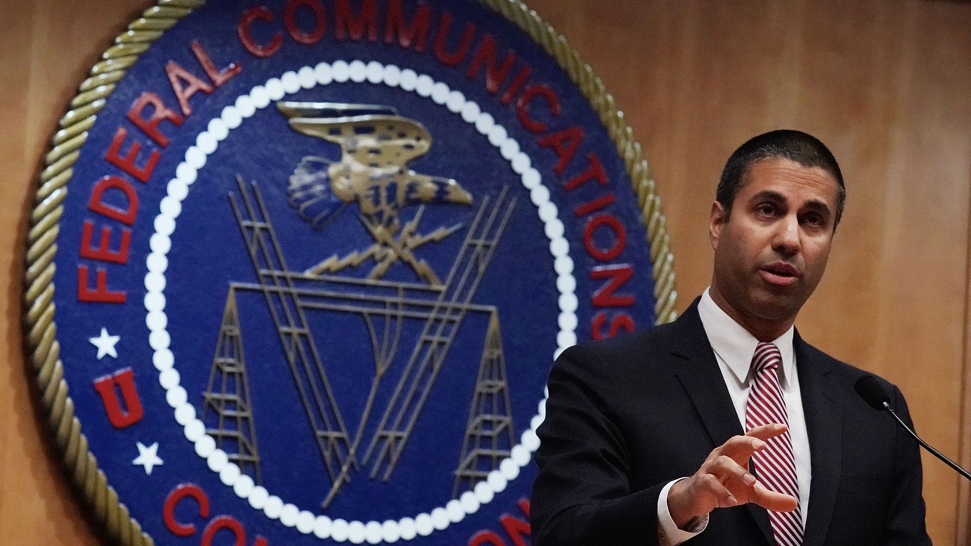 A photo of FCC Chairman Ajit Pai standing and speaking in front of the FCC logo.