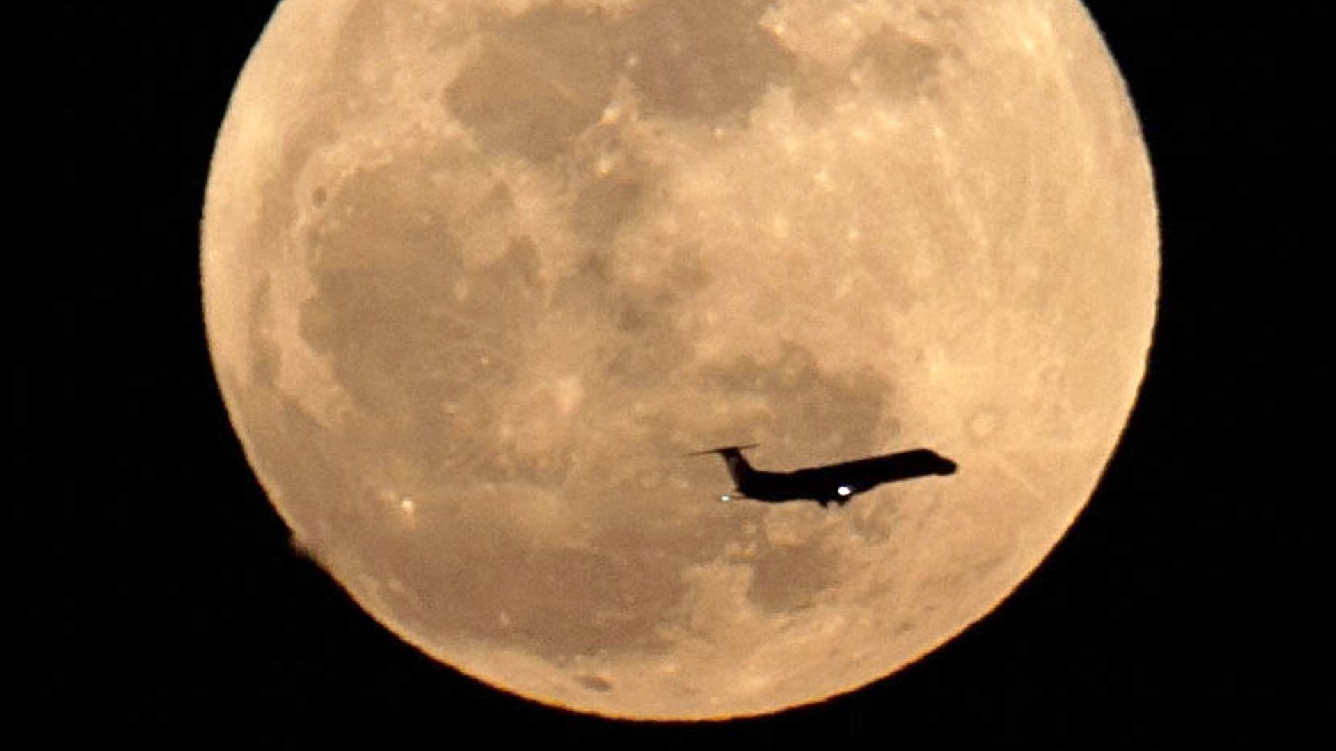 A plane flies in front of a golden full moon. 