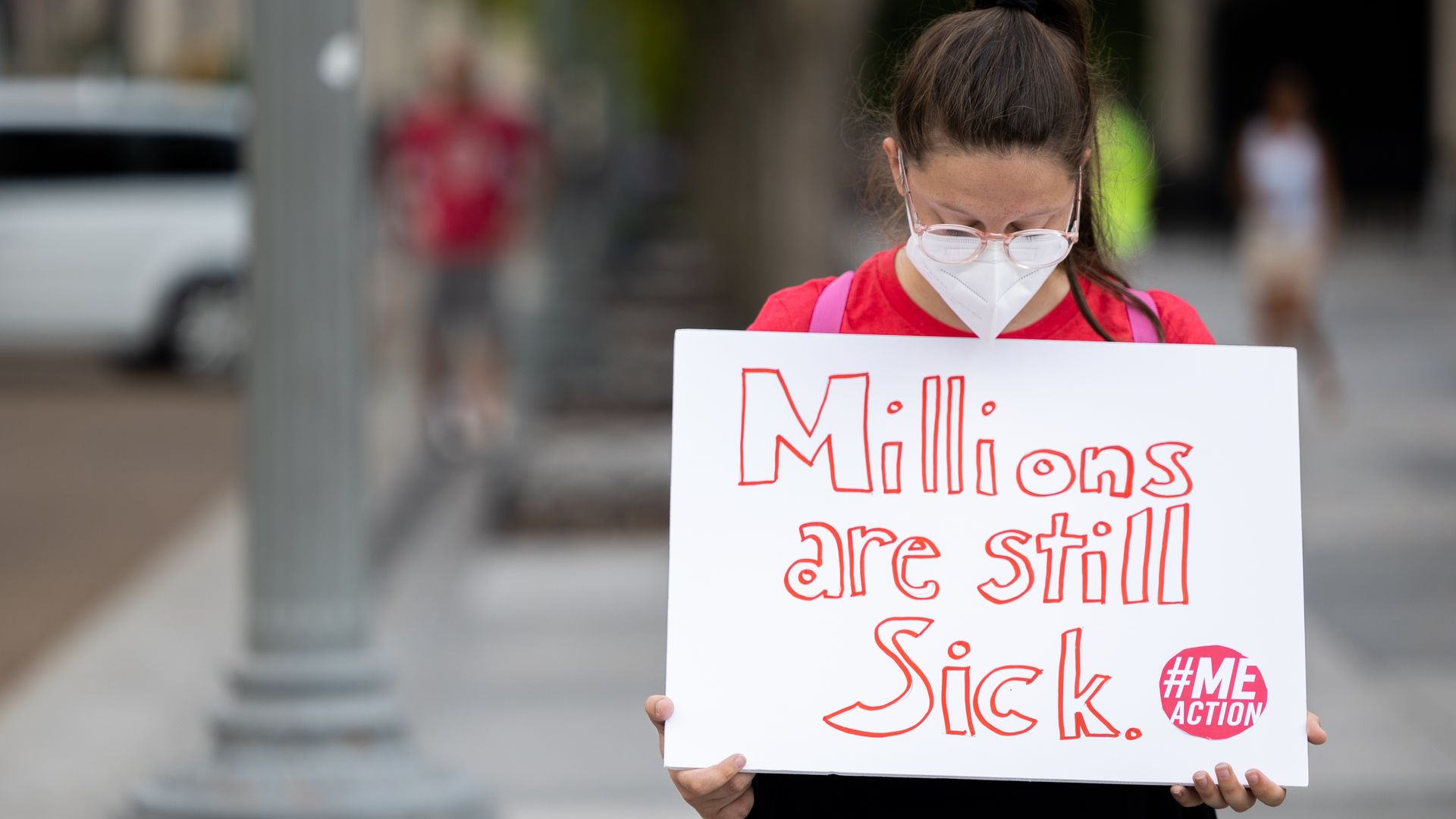 Person holding placard that says "Millions are still sick" in COVID demonstration outside White House