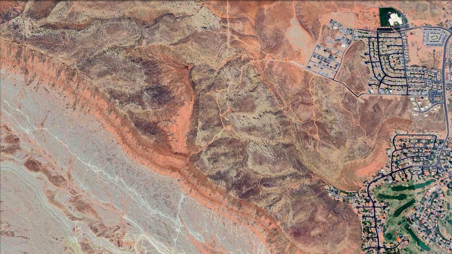 An aerial view of redrock desert next to a city.