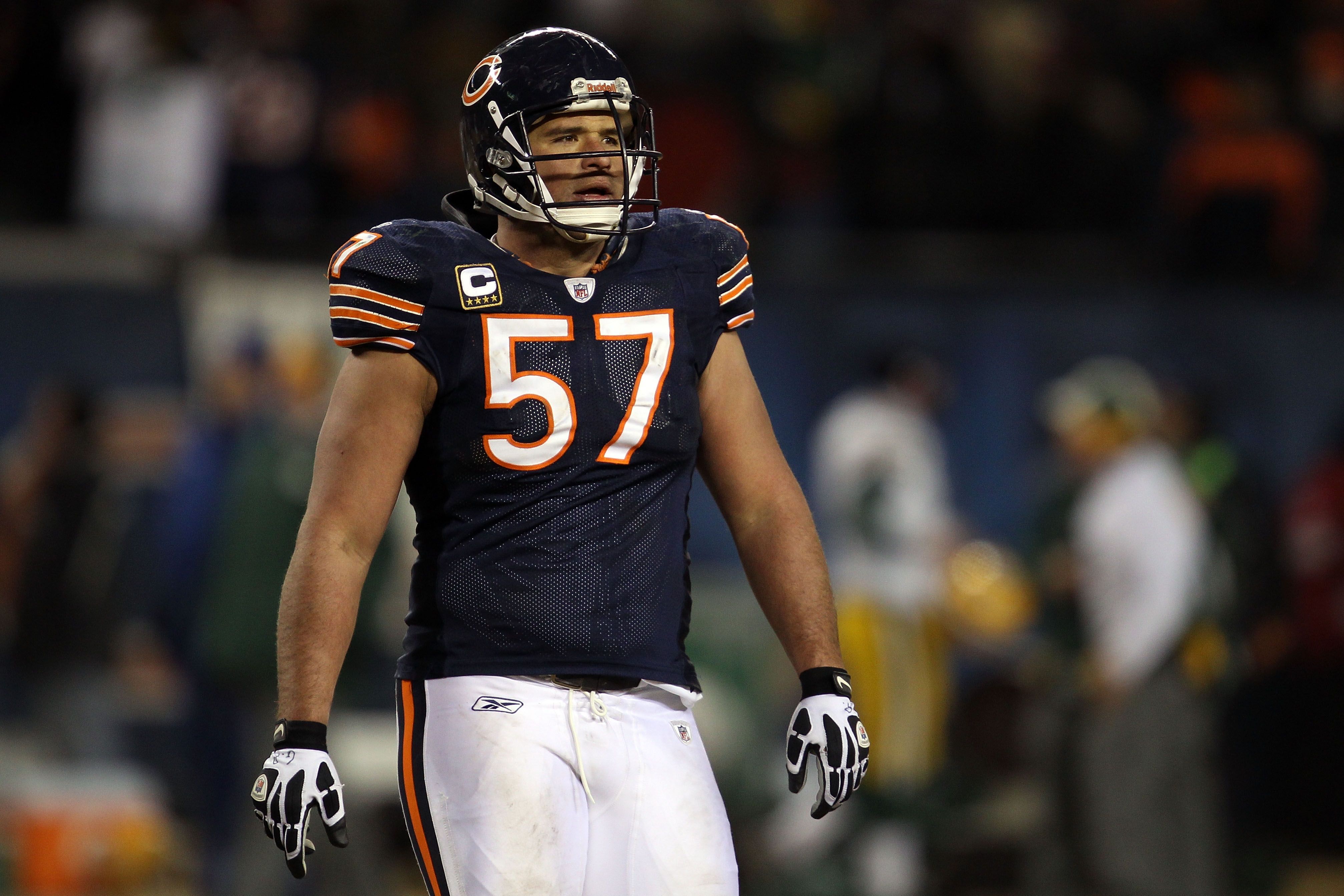 American football player in navy blue jersey number 57 with orange and white stripes, white pants, and helmet standing on field during game at night.
