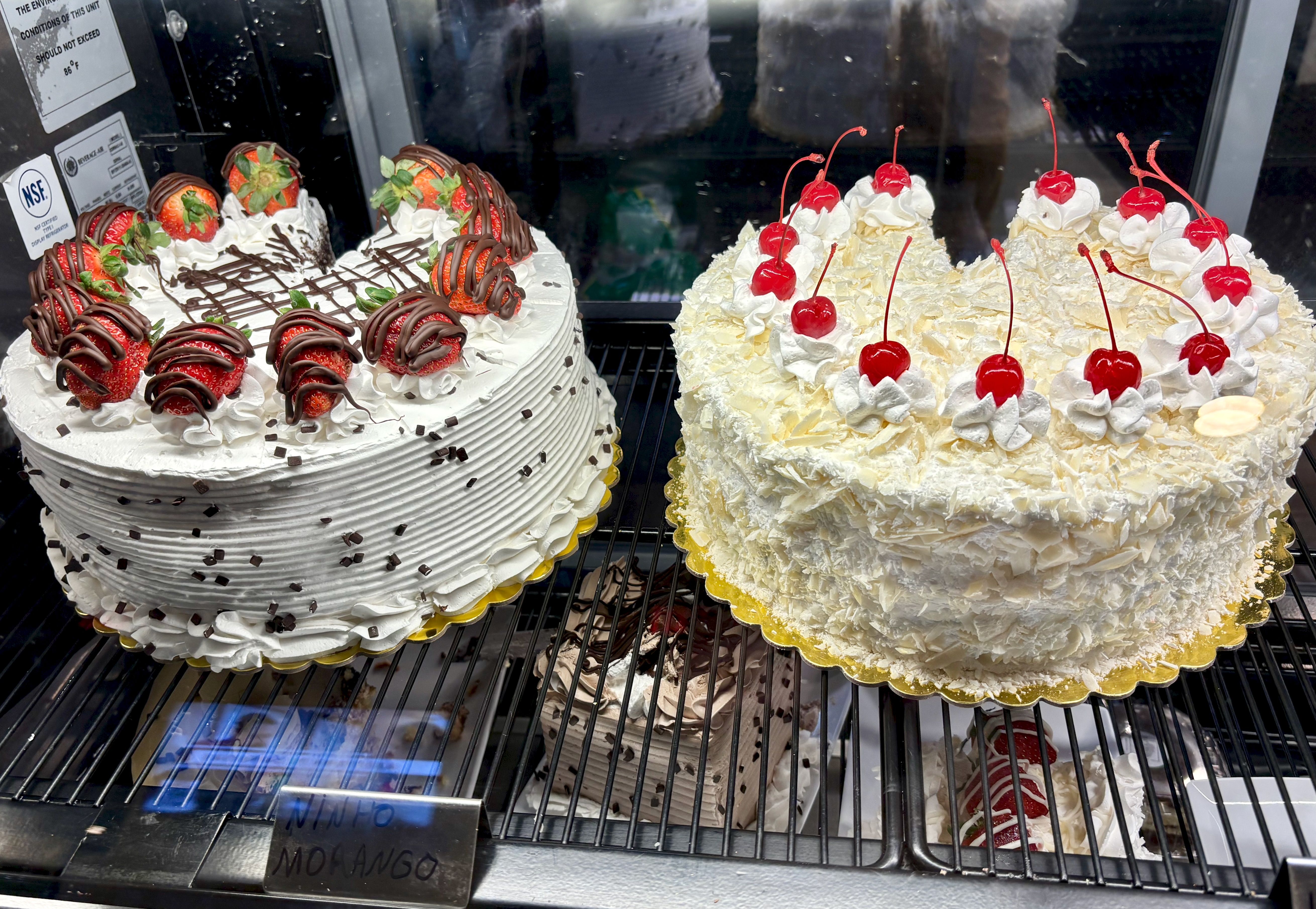 A close-up of two cakes, one topped with strawberries and one topped with cherries