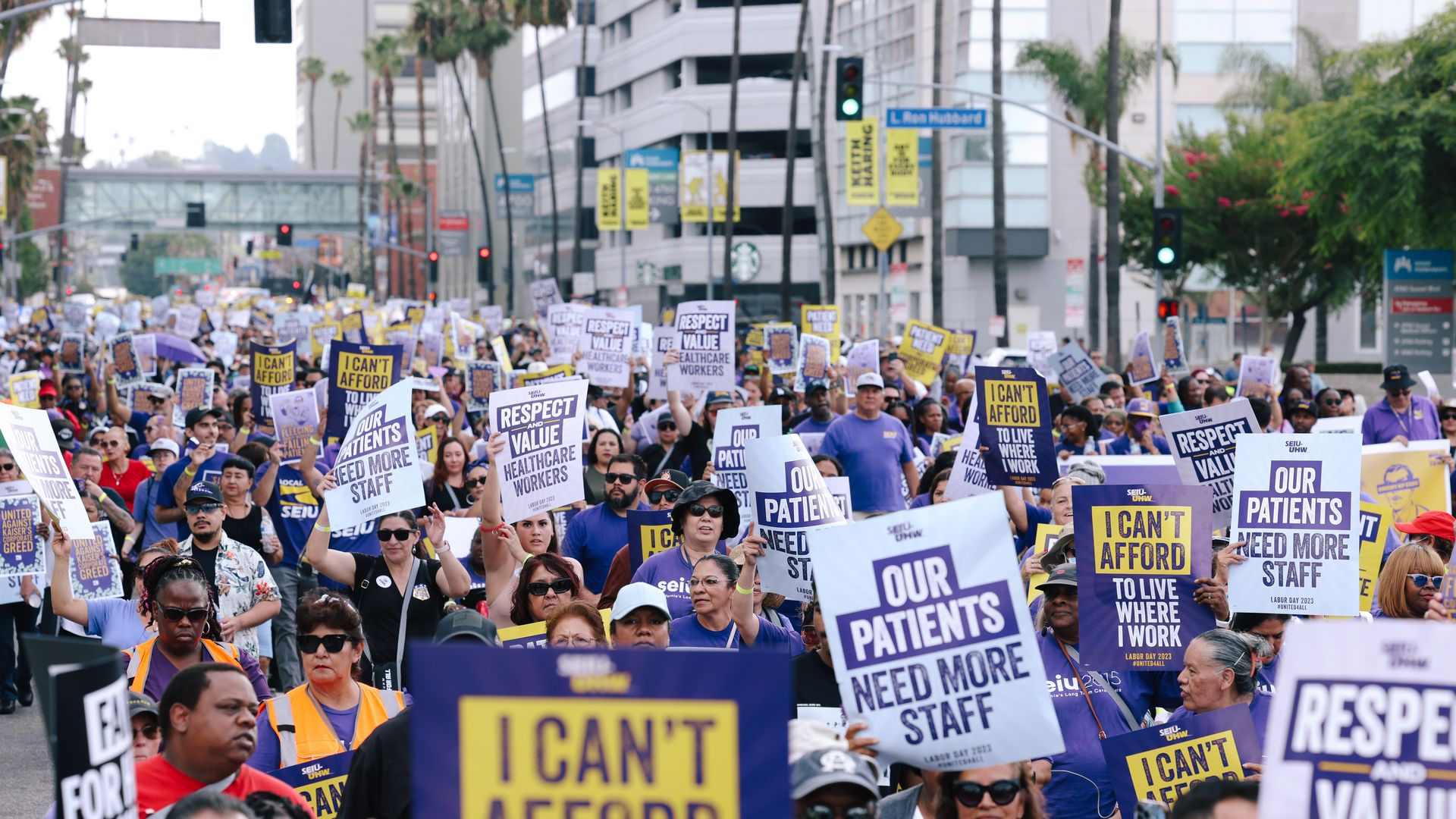 Thousands of healthcare workers march down the street in Los Angeles with signs protesting staffing and wages.