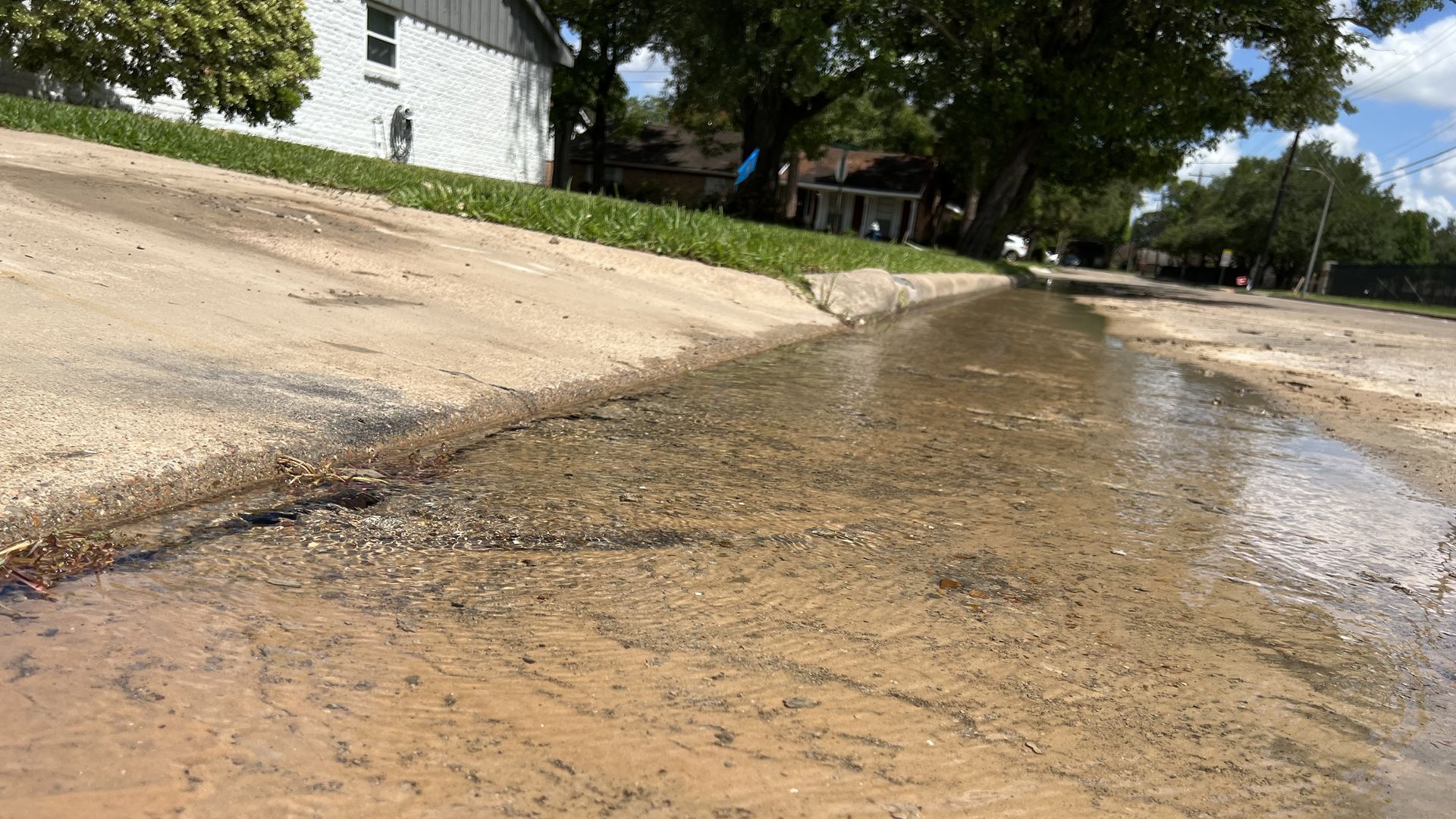 Close-up of water leaking from a broken underground water pipe in a residential Houston neighborhood on a sunny day