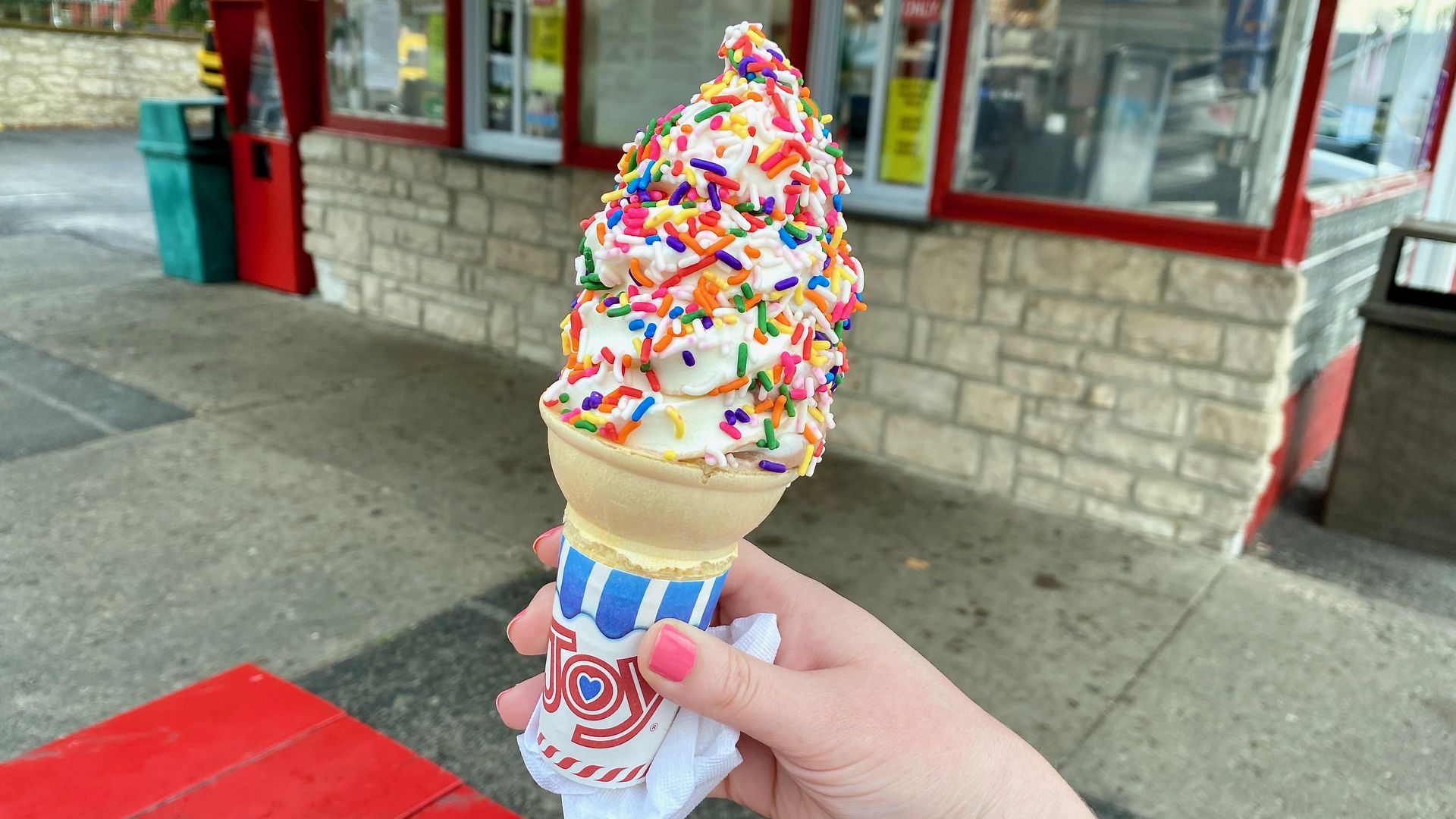 A soft serve ice cream cone covered in rainbow sprinkles