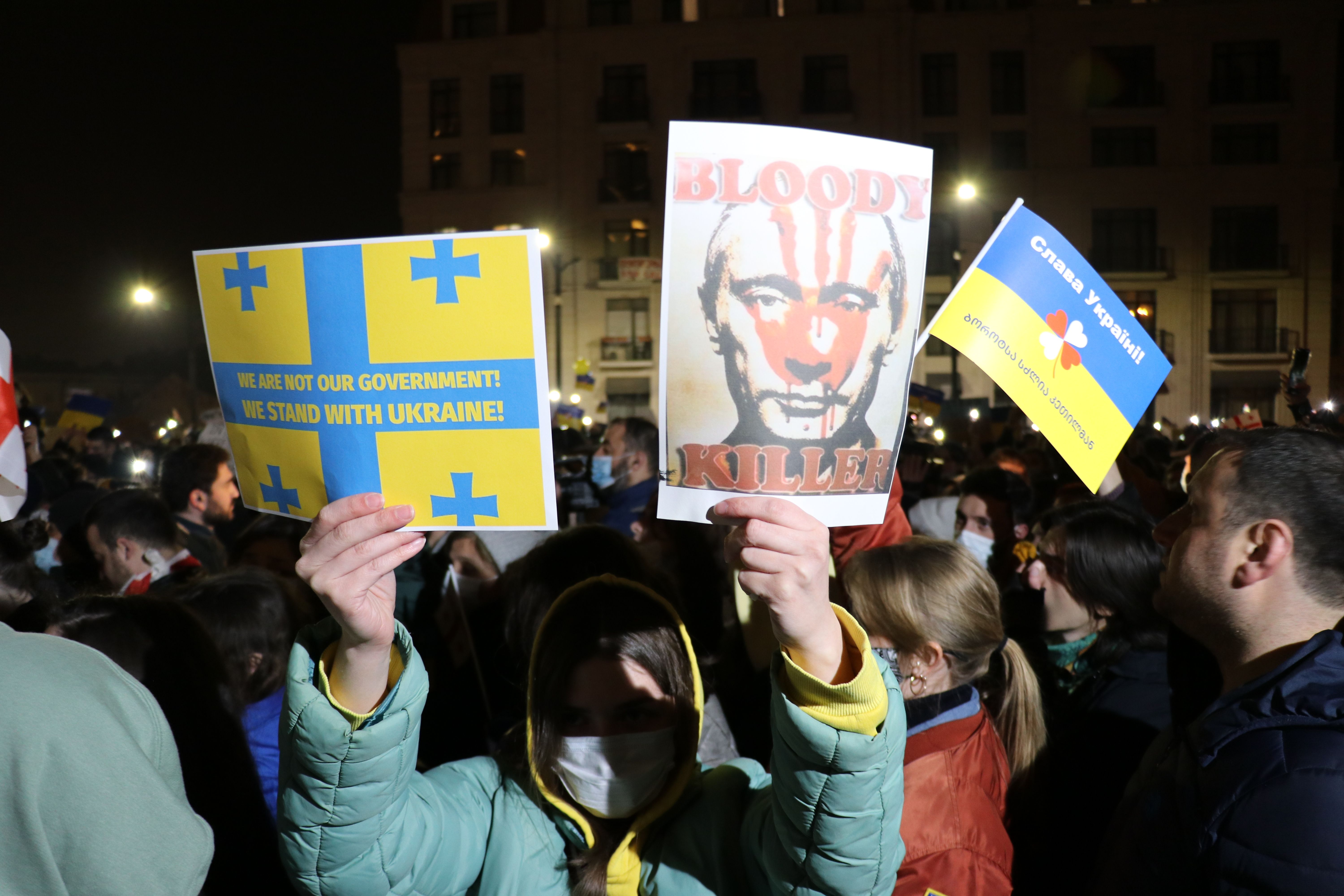 Photo of a protester holding a sign of the Ukraine flag and another that has the photo of Putin with the words "Bloody killer"