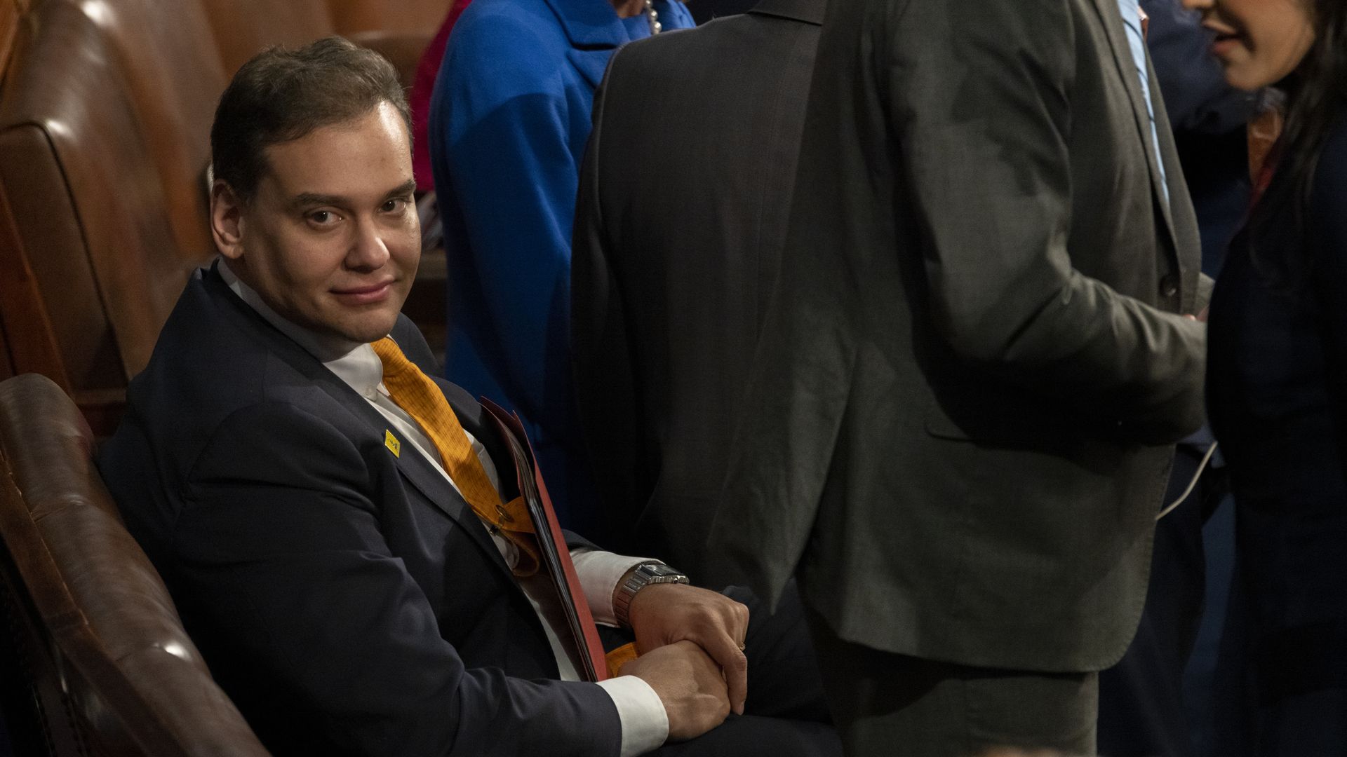 Rep. George Santos, wearing a gray suit, white shirt and orange tie, sits in the House chamber.