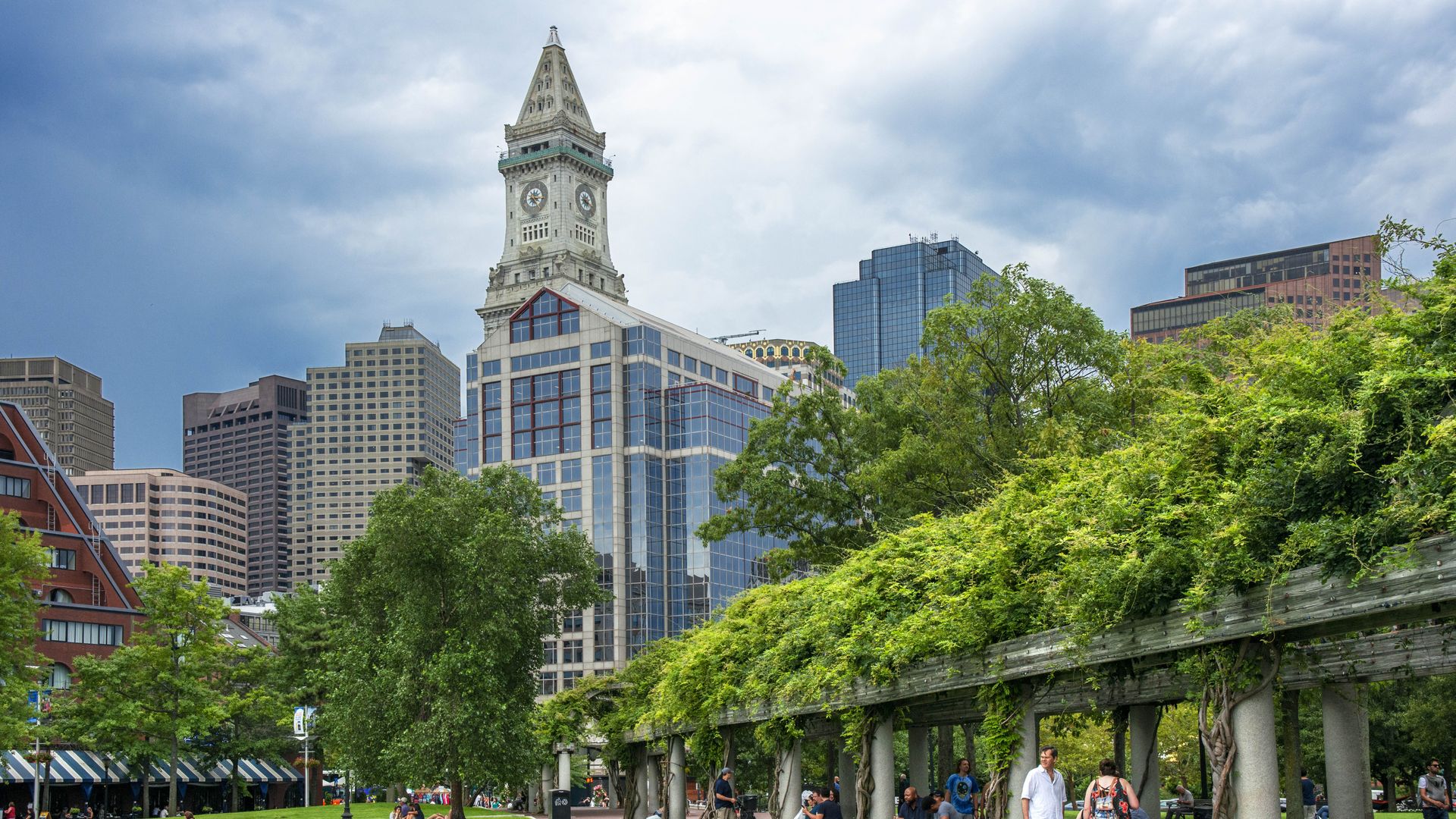 View of Boston’s Financial District with the historic Custom House Tower in the center, photographed from Christopher Columbus Waterfront Park with green lawn in the foreground.