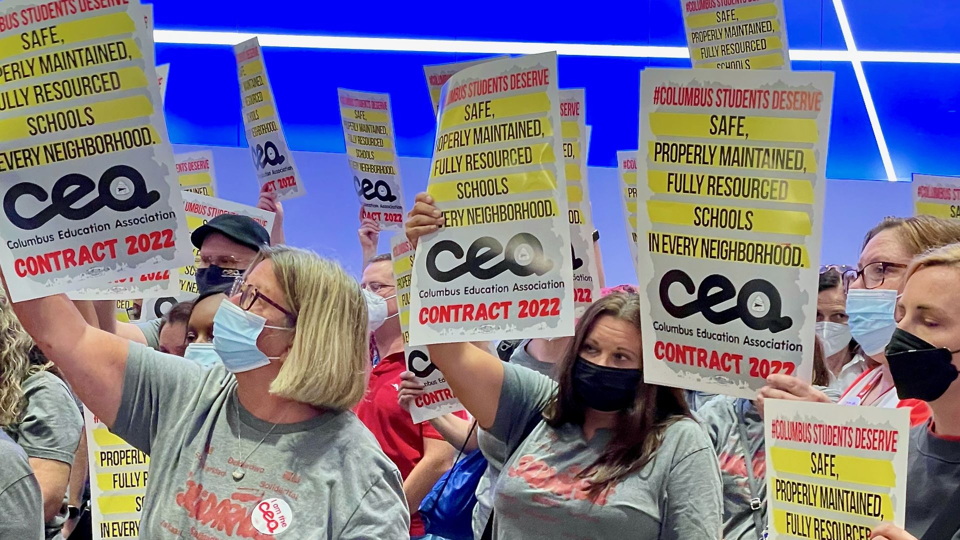 Teachers hold signs  that say "Columbus students deserve safe, properly maintained, fully resourced schools in every neighborhood. Columbus Education Association contract 2022"