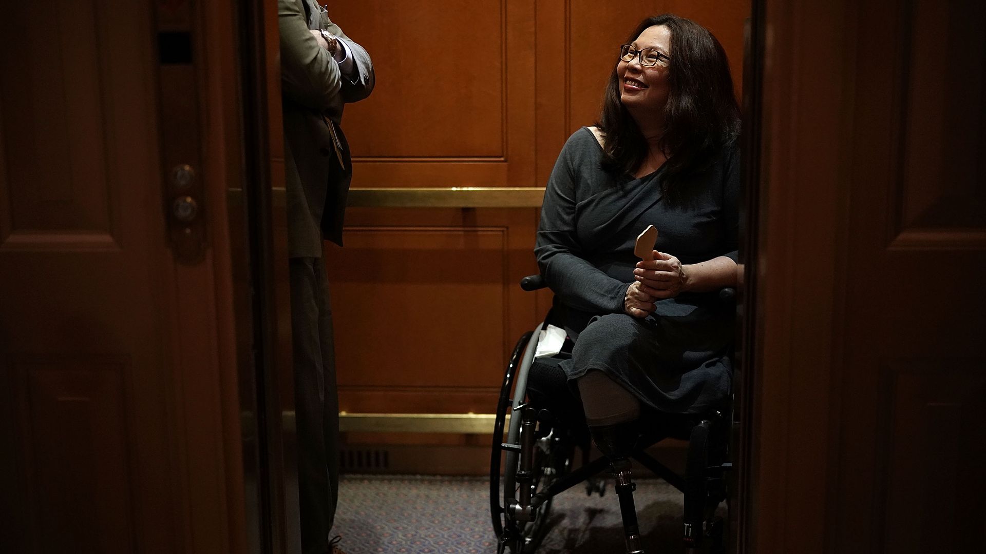 Tammy Duckworth smiles up from her wheelchair while in an elevator