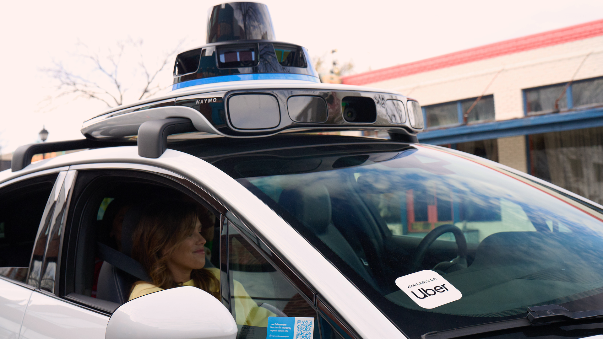 A photo of a person in a Waymo car with a stick on the windshield that reads "Uber."