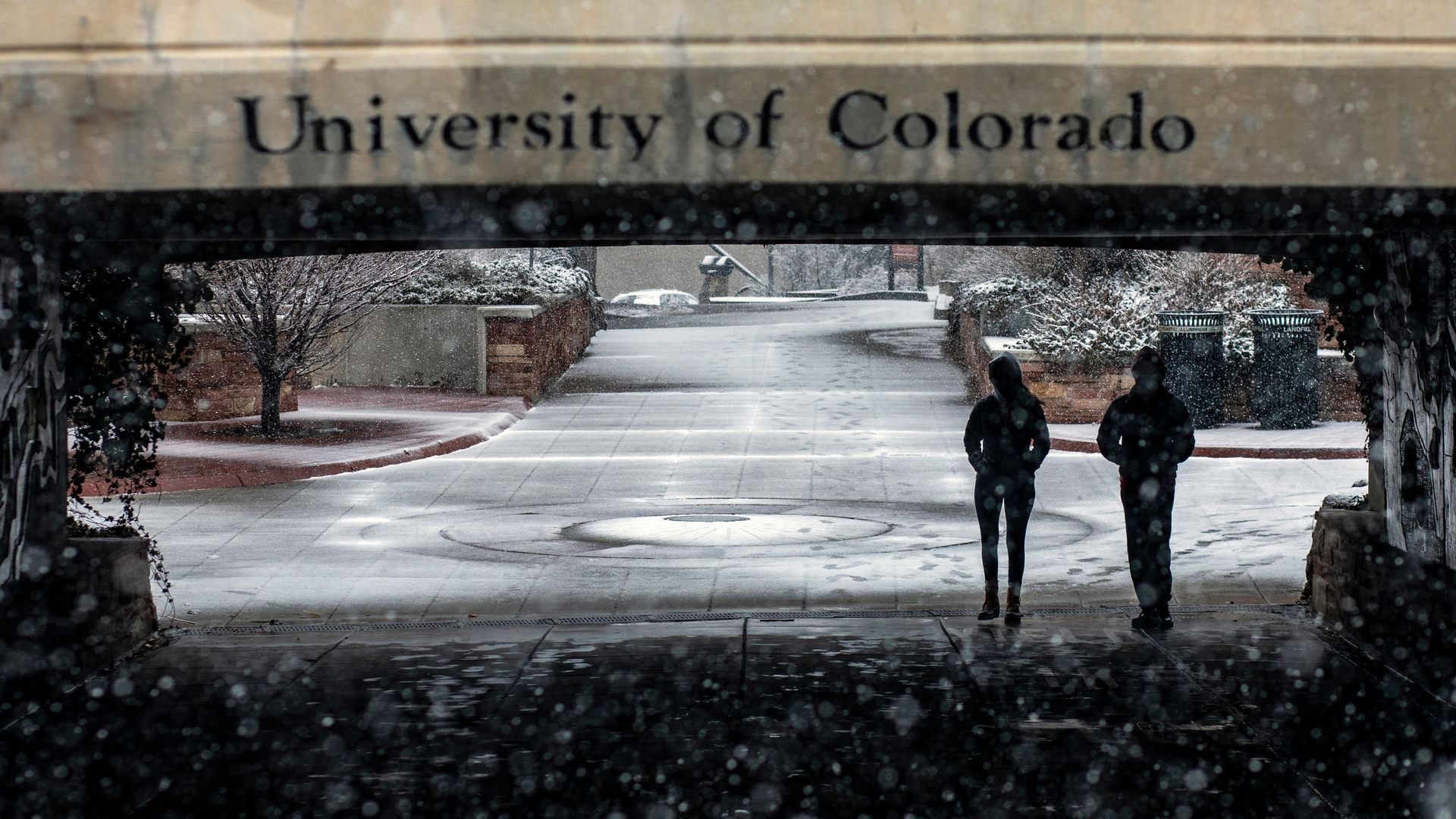 Two people walk in an underpass with the words UNIVERSITY OF COLORADO above it.