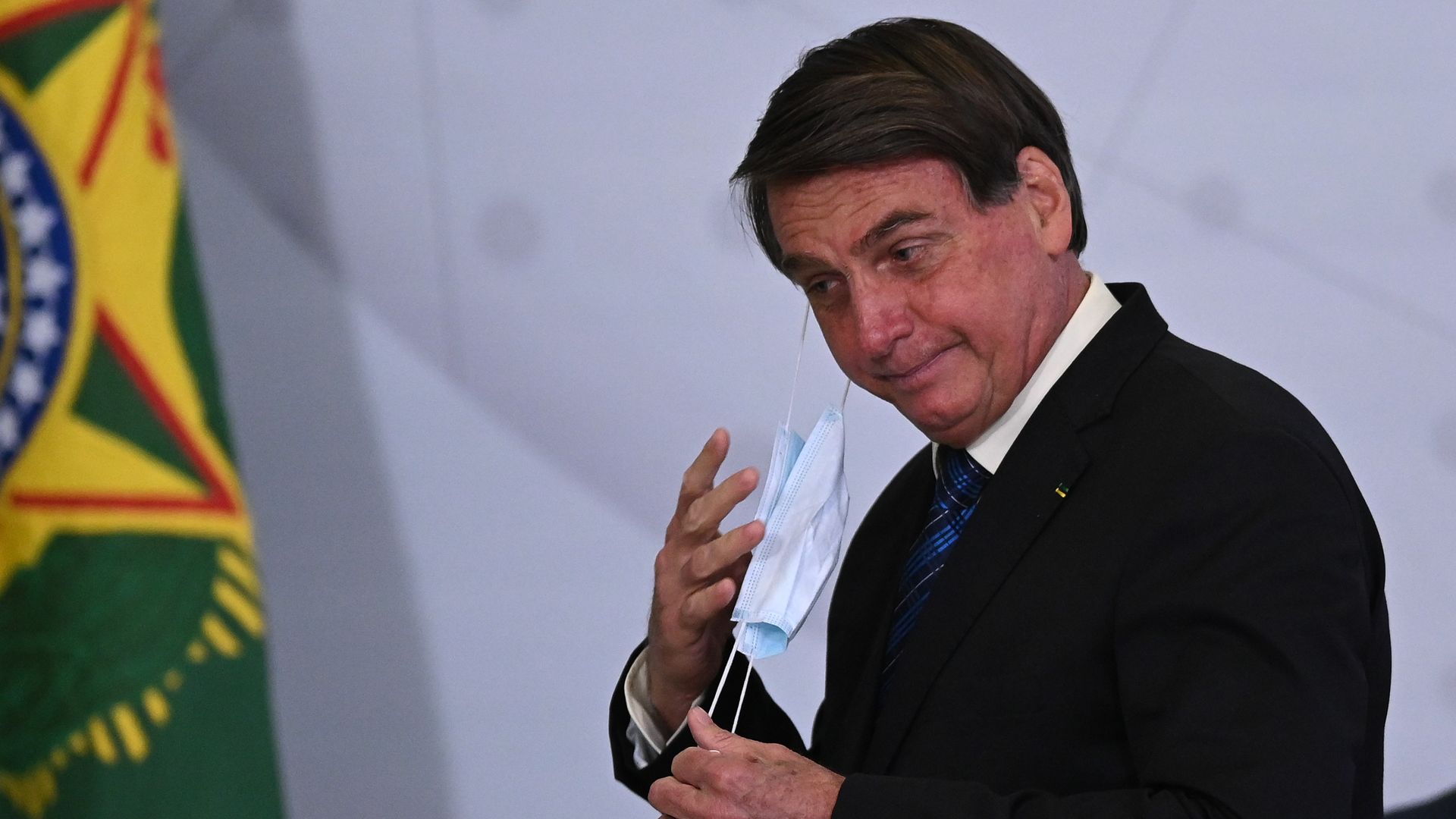 Jair Bolsonaro, President of Brazil, takes off his protective mask before speaking at an event at the Presidential Palace