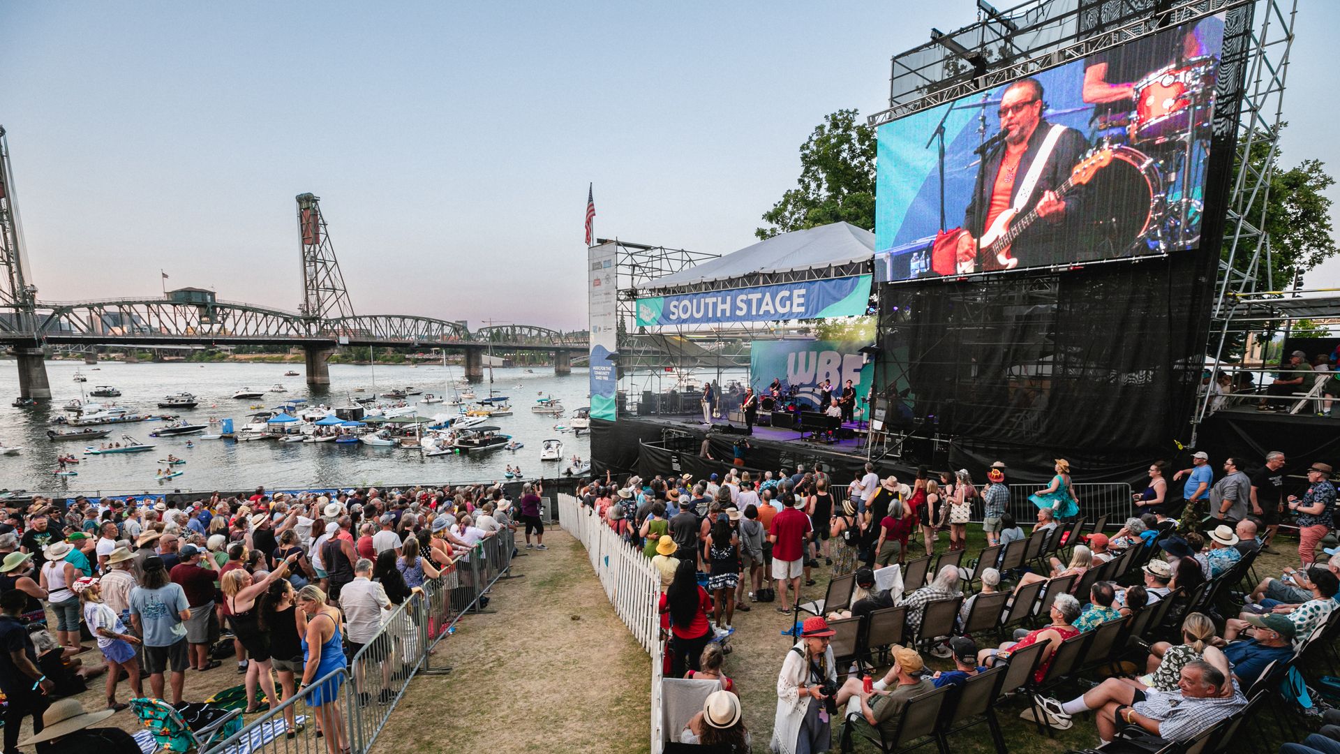 music festival crowd by river with bridge and stage