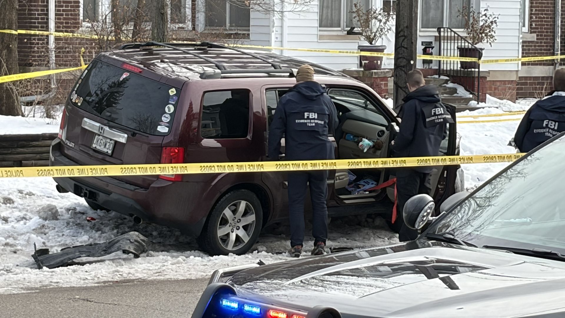 FBI agents wearing blue jackets search through a maroon Honda Pilot, with police tape around them. 