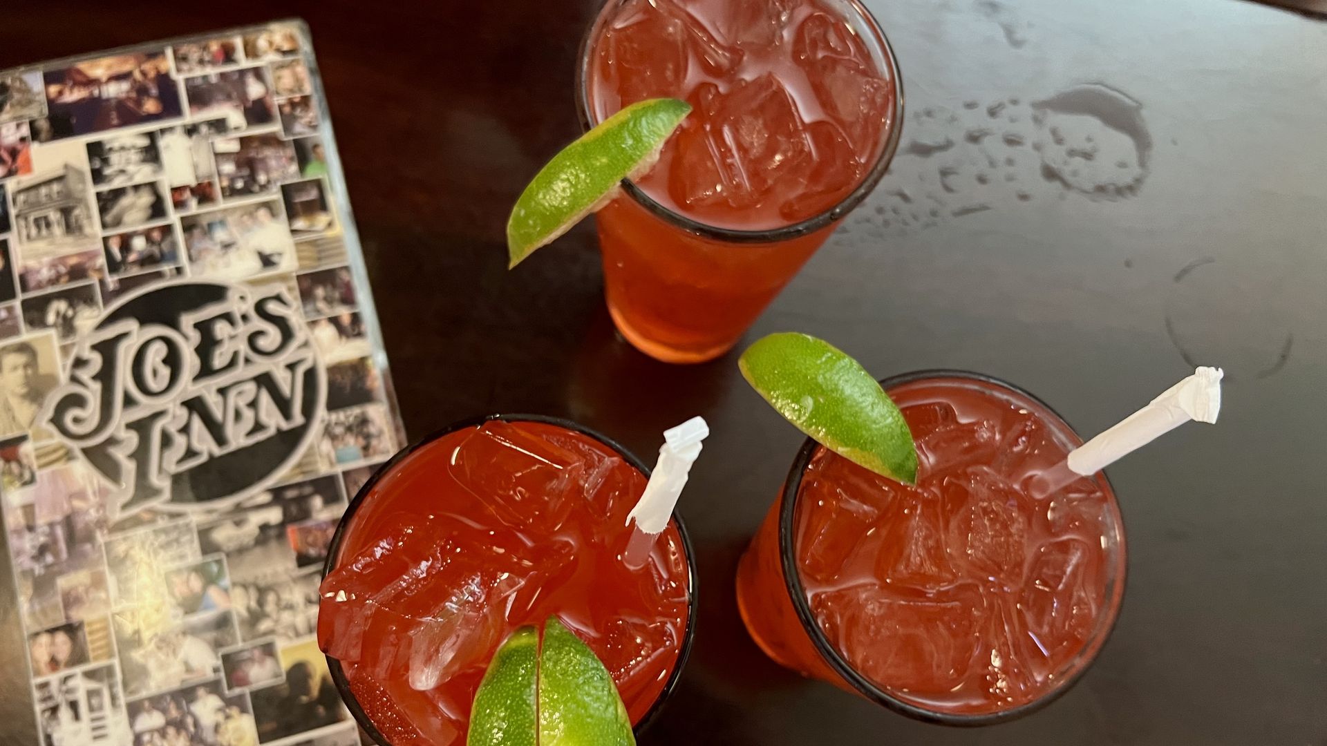 A menu that says "joe's inn" on the left and three tall clear glasses with red liquid, a straw, and limes