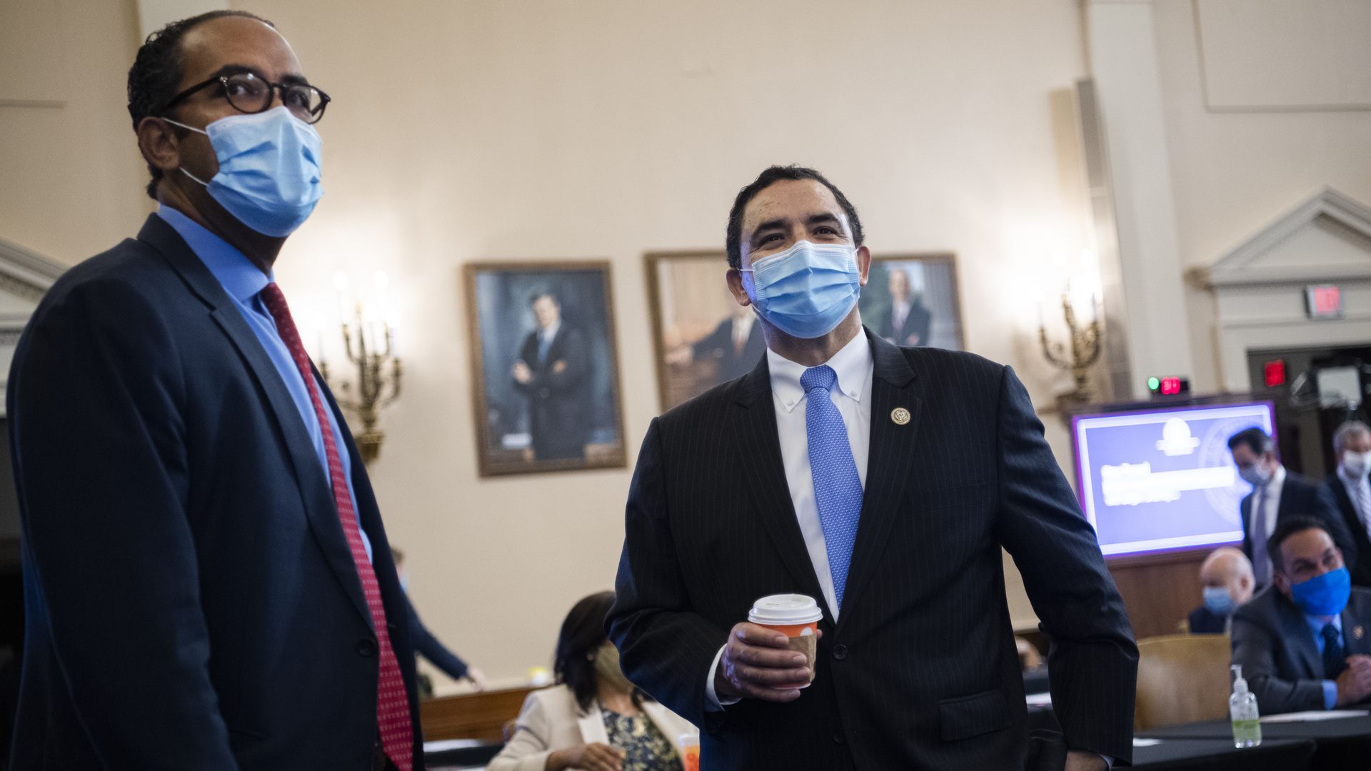 Rep. Henry Cuellar standing holding a cup of coffee with a mask and blue tie. 