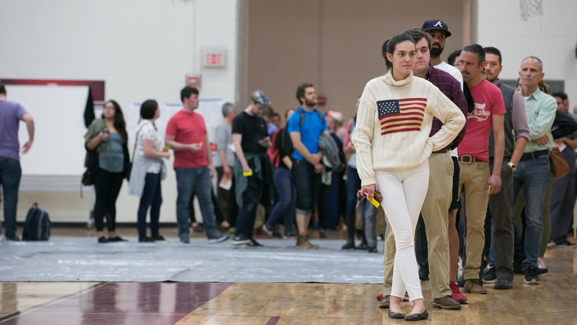 Voters in line to vote, woman in all white with flag on shirt.