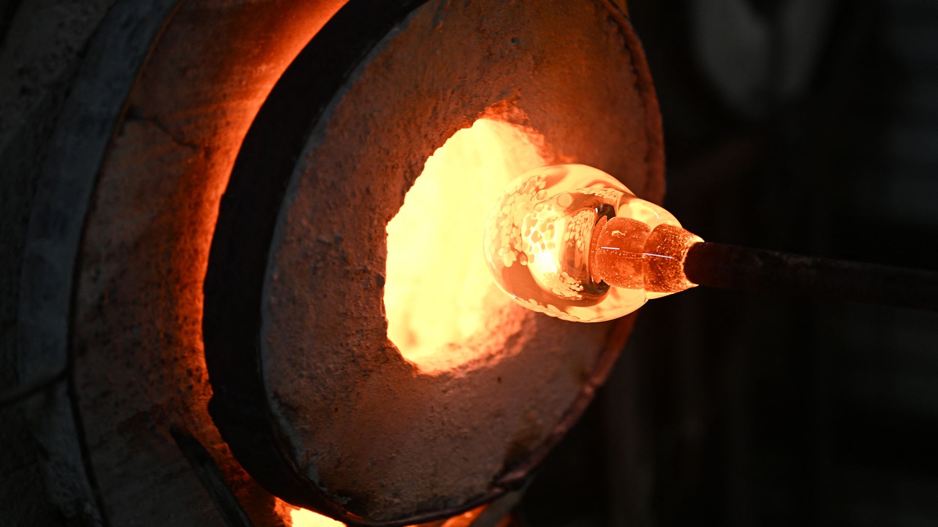 Molten yellow-orange glass on a rod going into a white-hot oven.