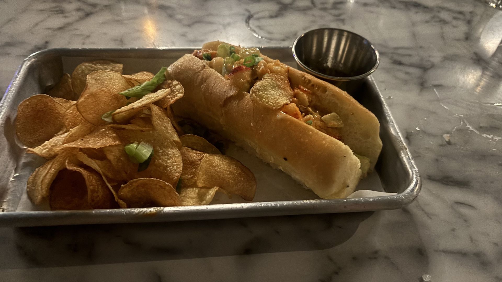 A lobster roll served on a metal tray with house made chips