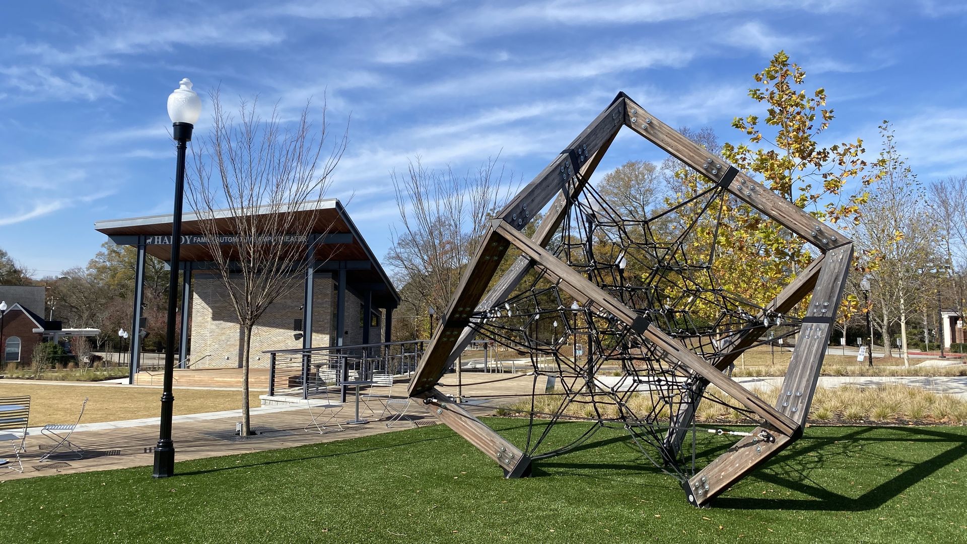 A piece of playground climbing equipment shaped like a cube and a stage in a downtown square