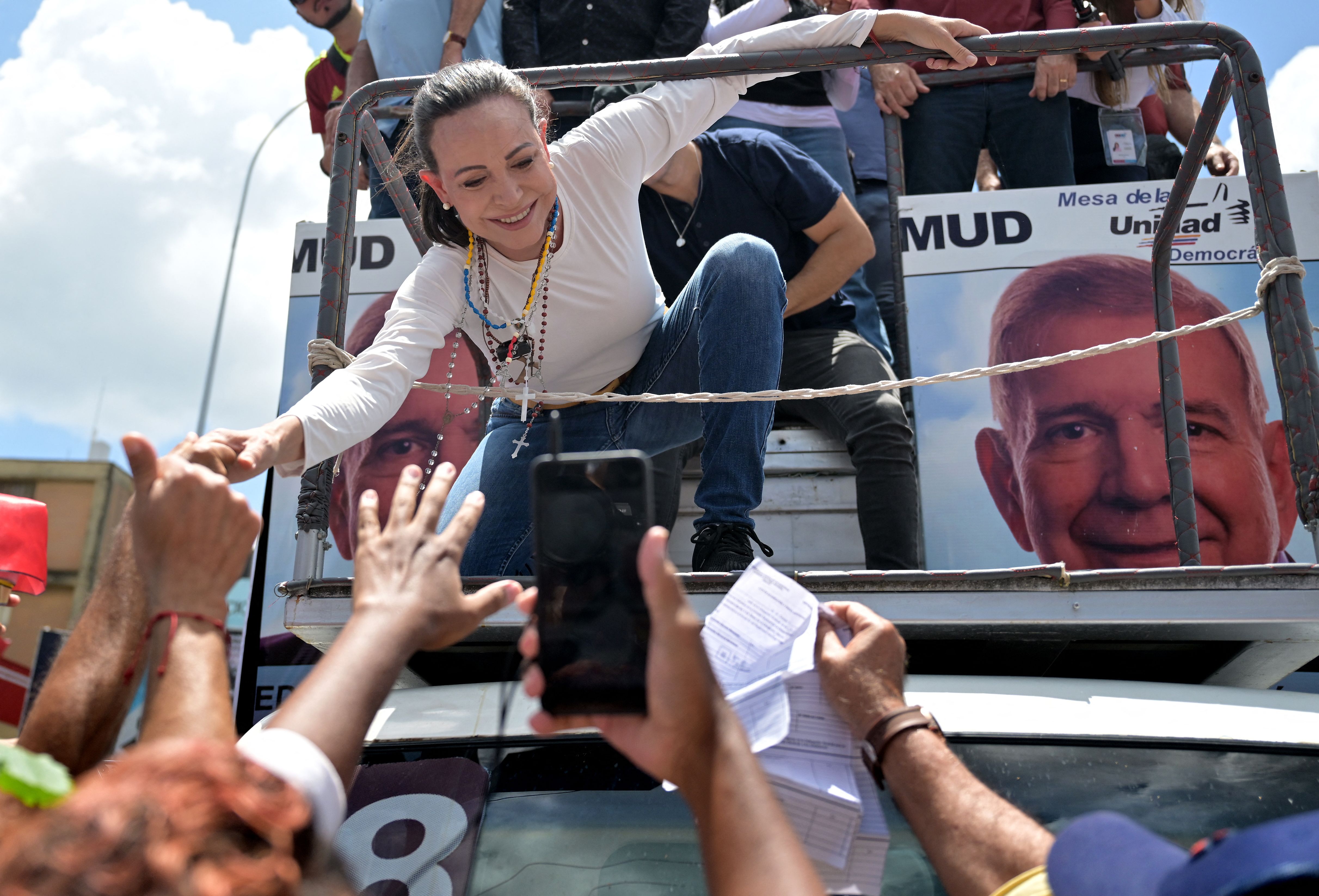 Maria Corina Machado, an opposition leader, crouches down and shakes hands with protesters while atop a truck during a protest in Caracas, Venezuela against Maduro