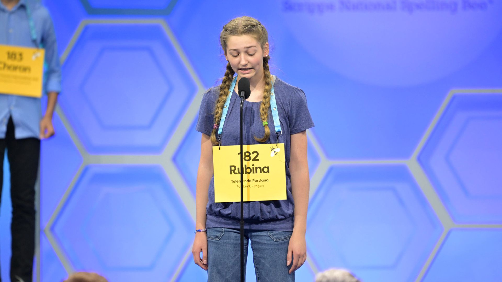 A photo of a person standing and speaking into a microphone on a stand.
