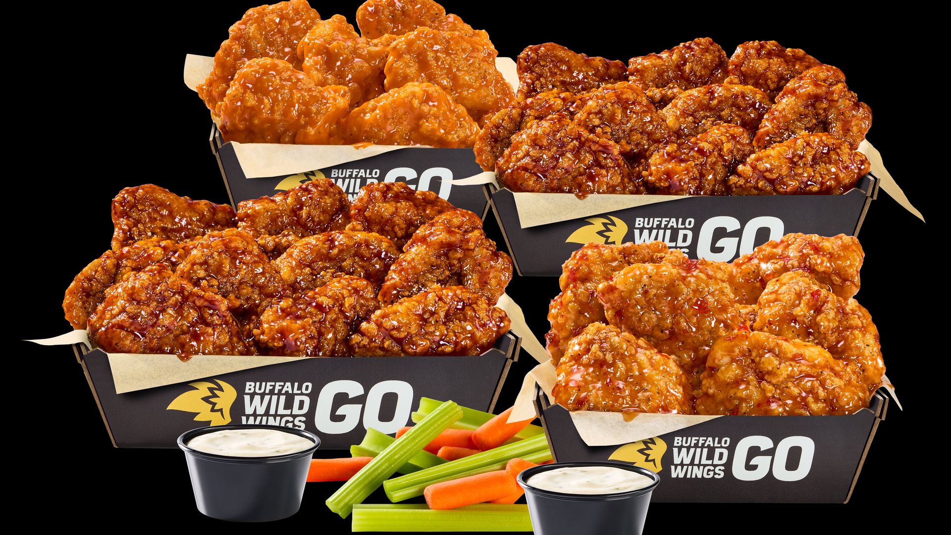 Assorted Buffalo Wild Wings Go boxes overflow with glossy, orange-glazed fried chicken wings, surrounded by dipping sauces and celery and carrot sticks on a black background.