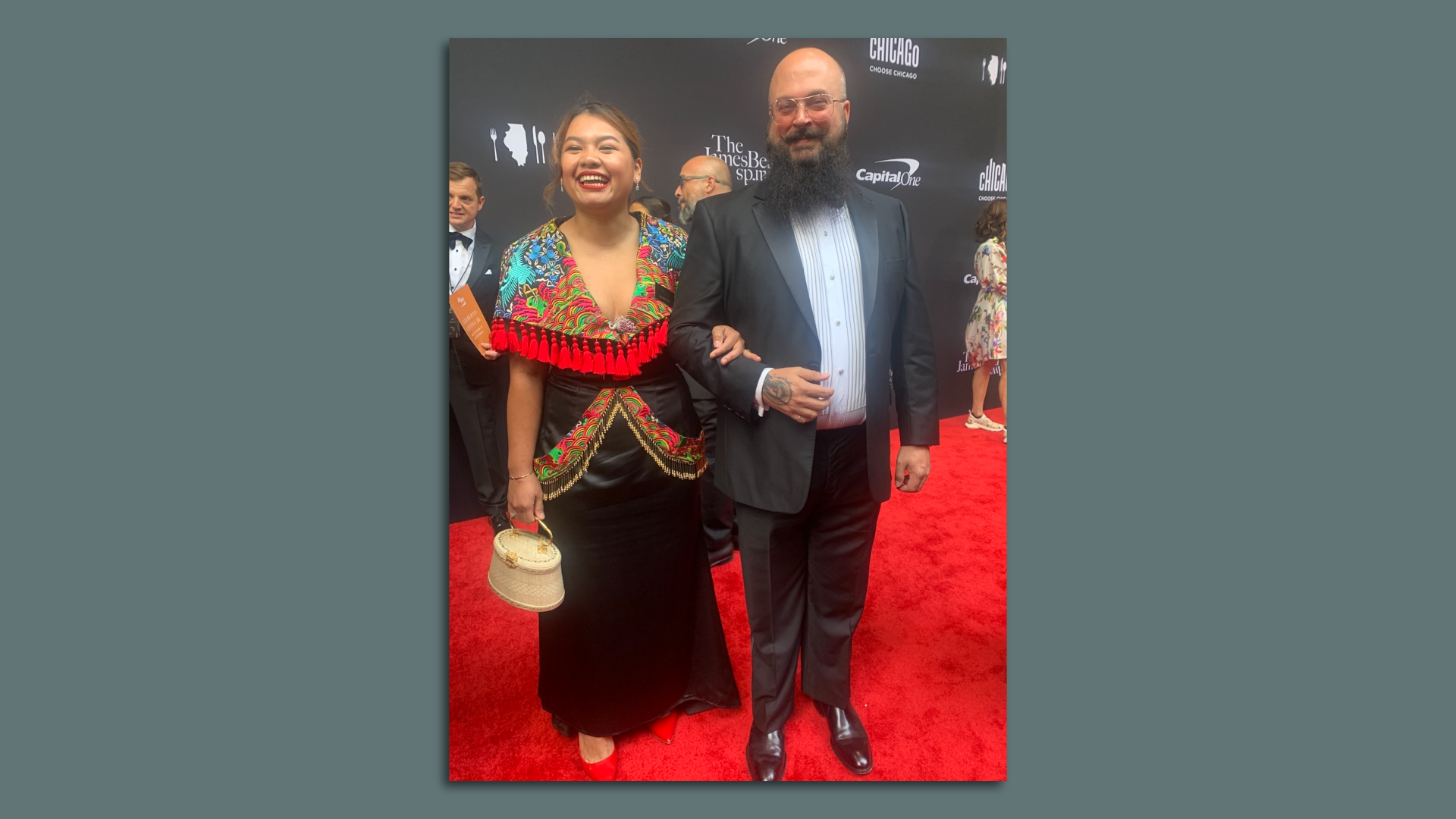 Benchawan Jabthong Painter from Houston laughs on the red carpet wearing a black dress, with colorful shawl, arm in arm with her date.