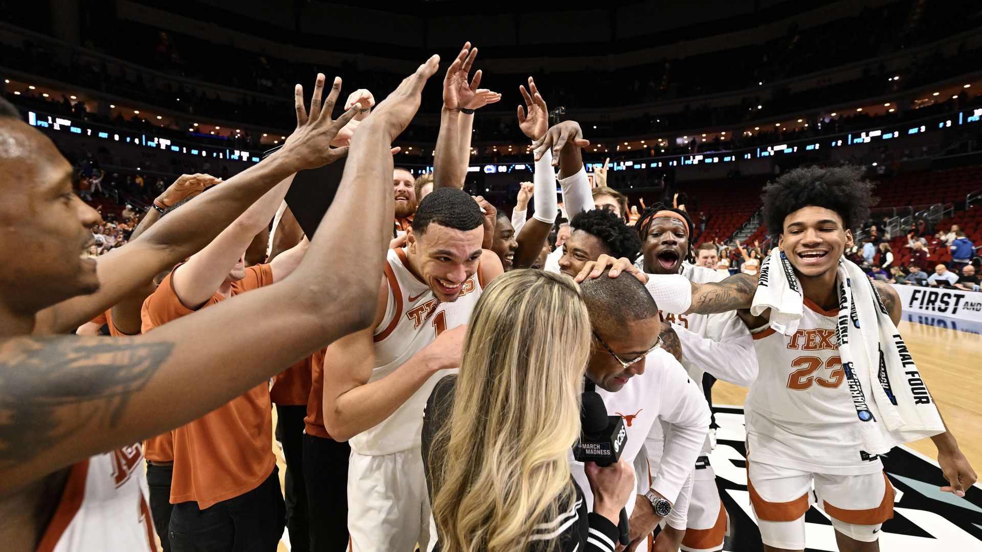 UT men's basketball players celebrate a victory with their coach as he's interviewed.