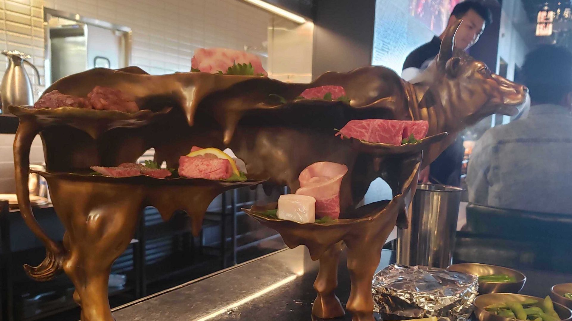 Bronze cow sculpture with various cuts of meat placed on it.