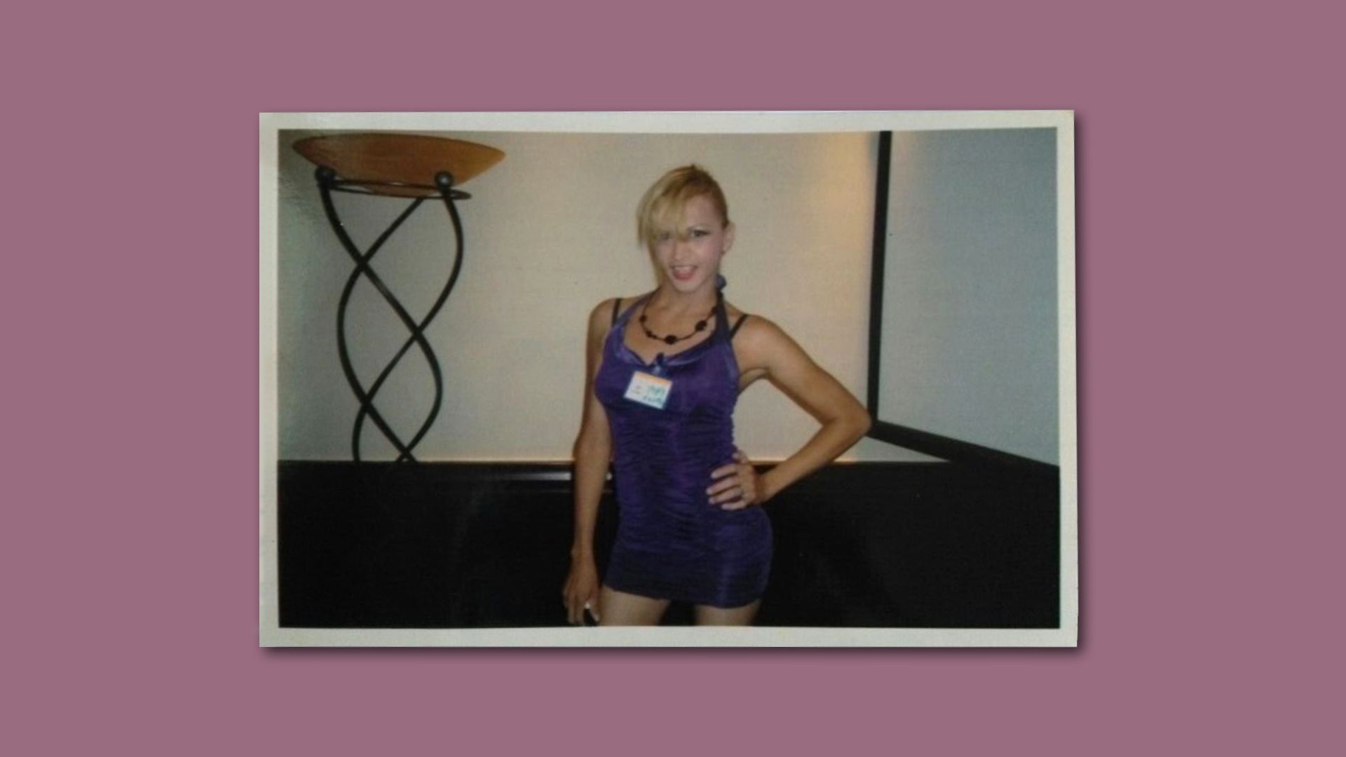 A photo of Vicky Hernandez wearing a dress and posing, against a pink background