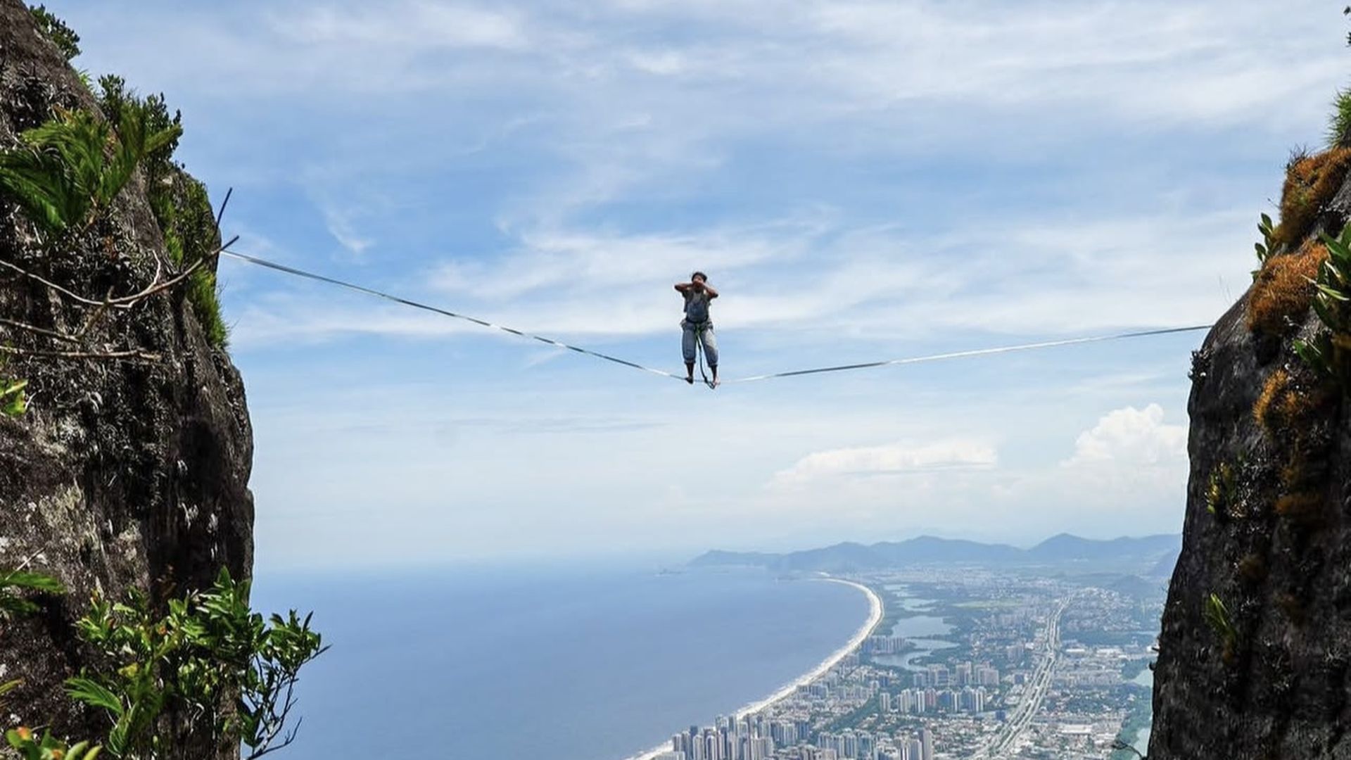 Photo of a person standing on a slackline between two mountains that overlook a cityscape