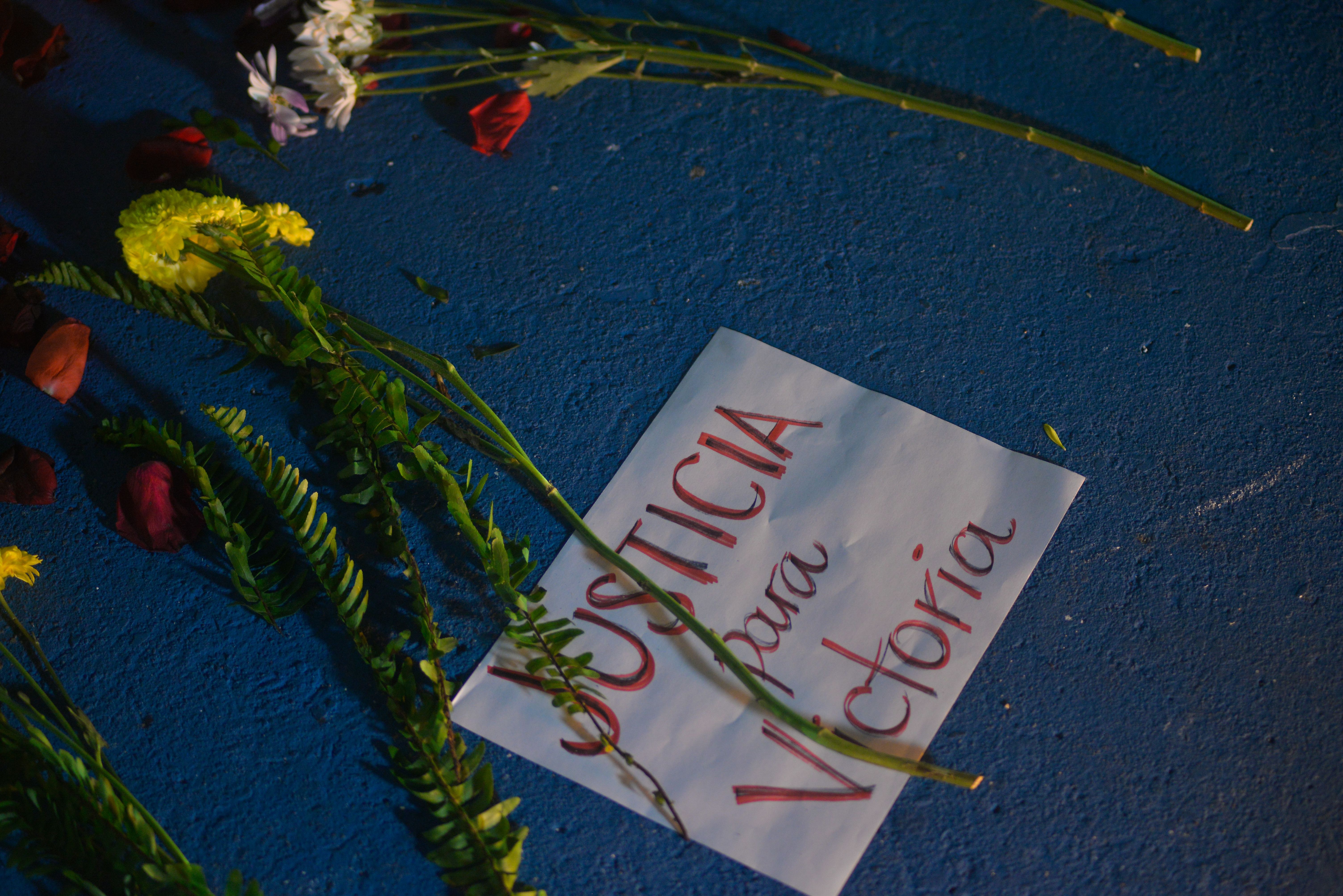 Photo of a sign on the ground that reads "Justicia para Victoria" with flowers laid around it