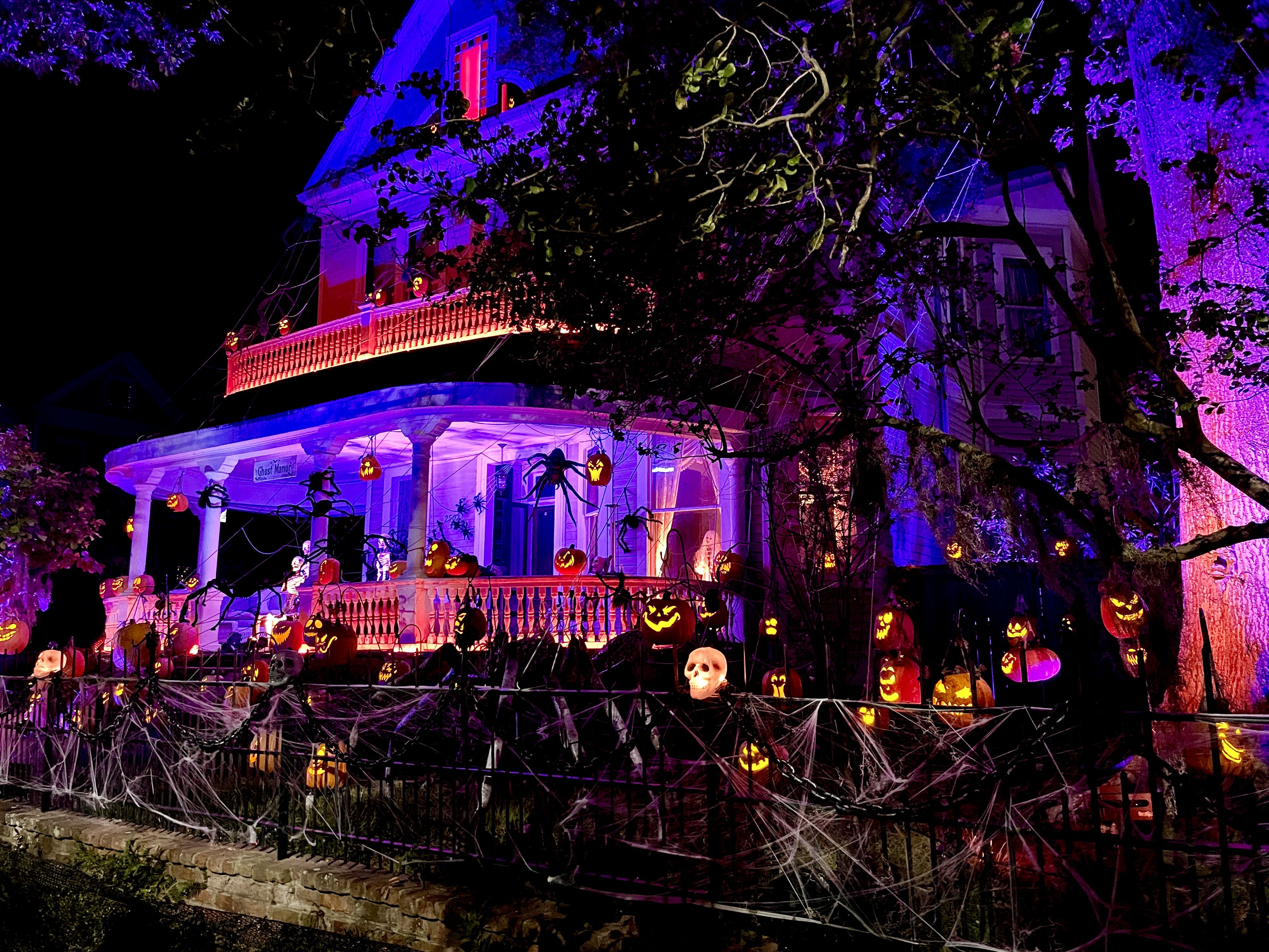 Photo shows a house lit up at night with pumpkins and skeletons