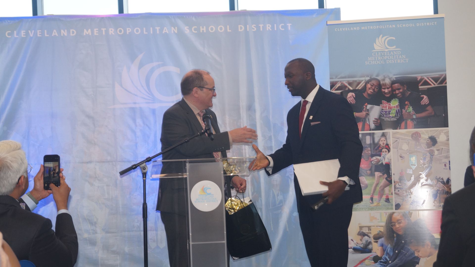 Eric Gordon (L) and Warren Morgan (R) shake hands in front of a Cleveland Metropolitan School District banner.