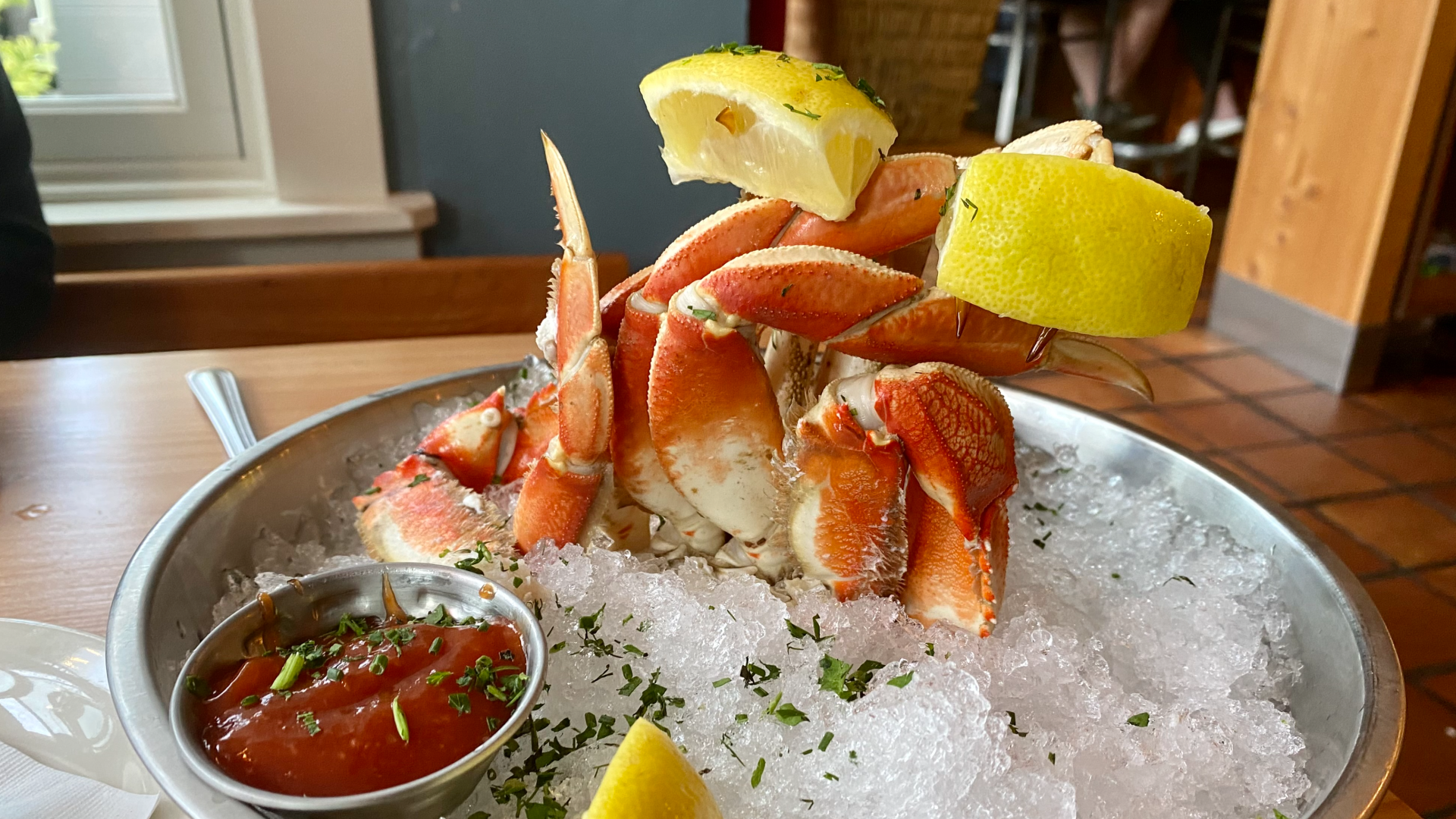 Crab legs sticking out of a bowl full of ice, garnished with lemon and a cocktail sauce dish on the side.