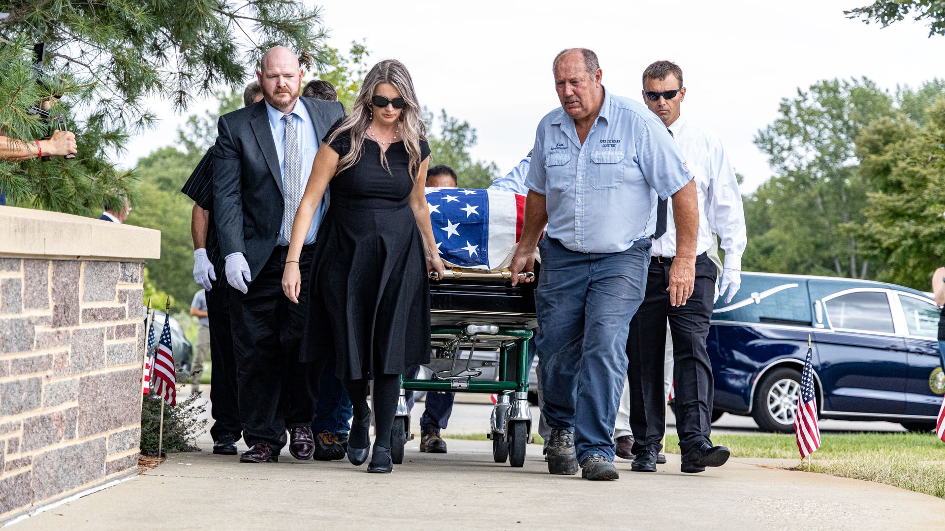 Lanae helping roll a casket, surrounded by men
